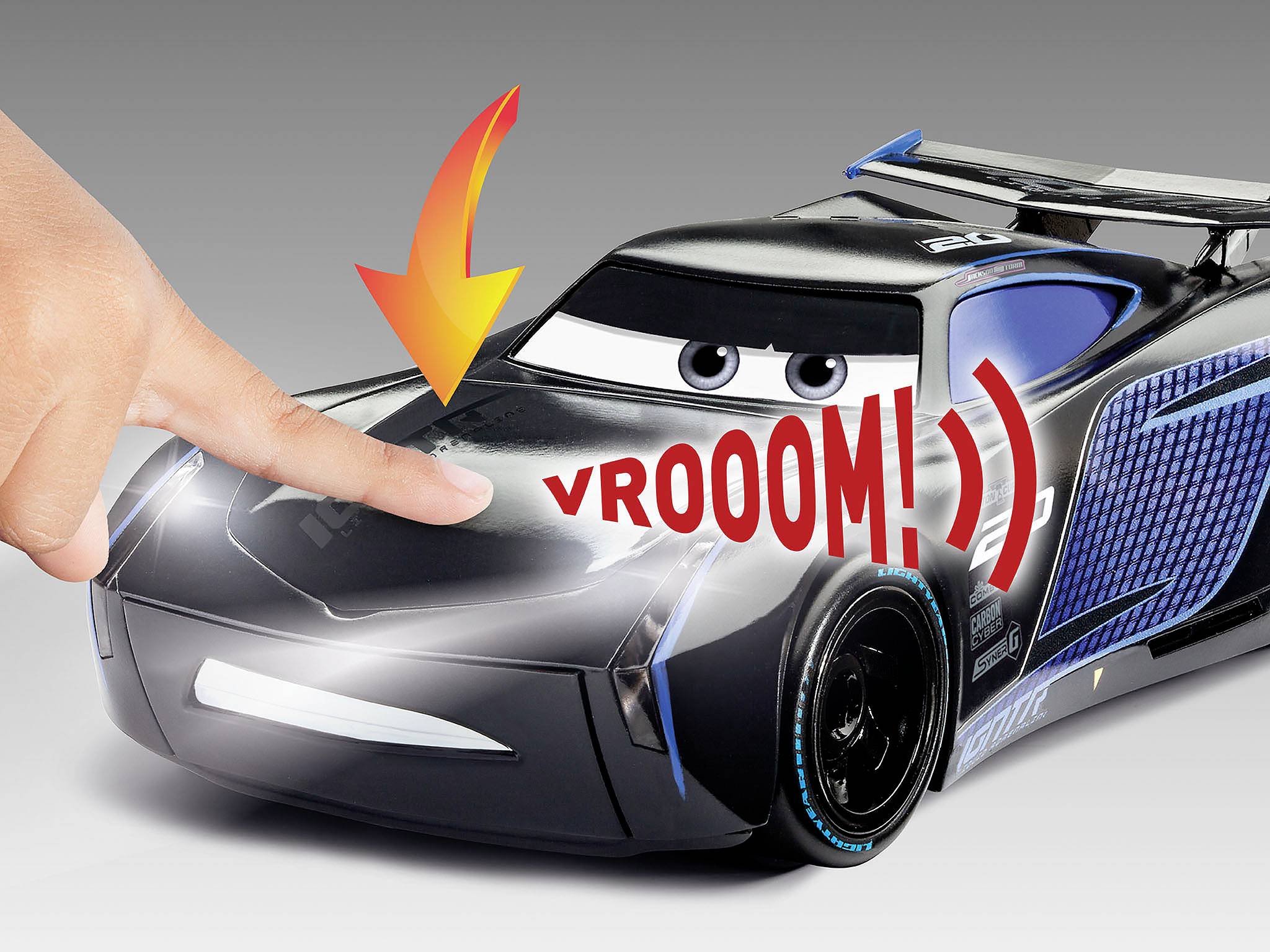 Prst tlačí na hračkárske autíčko s veľkými očami a textom 'VROOOM!'. Šípka ukazuje na miesto dotyku.