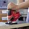 Osoba používa červenú elektrickú priamočiaru pílu na rezanie kusu dreva v dielni alebo kuchyni.