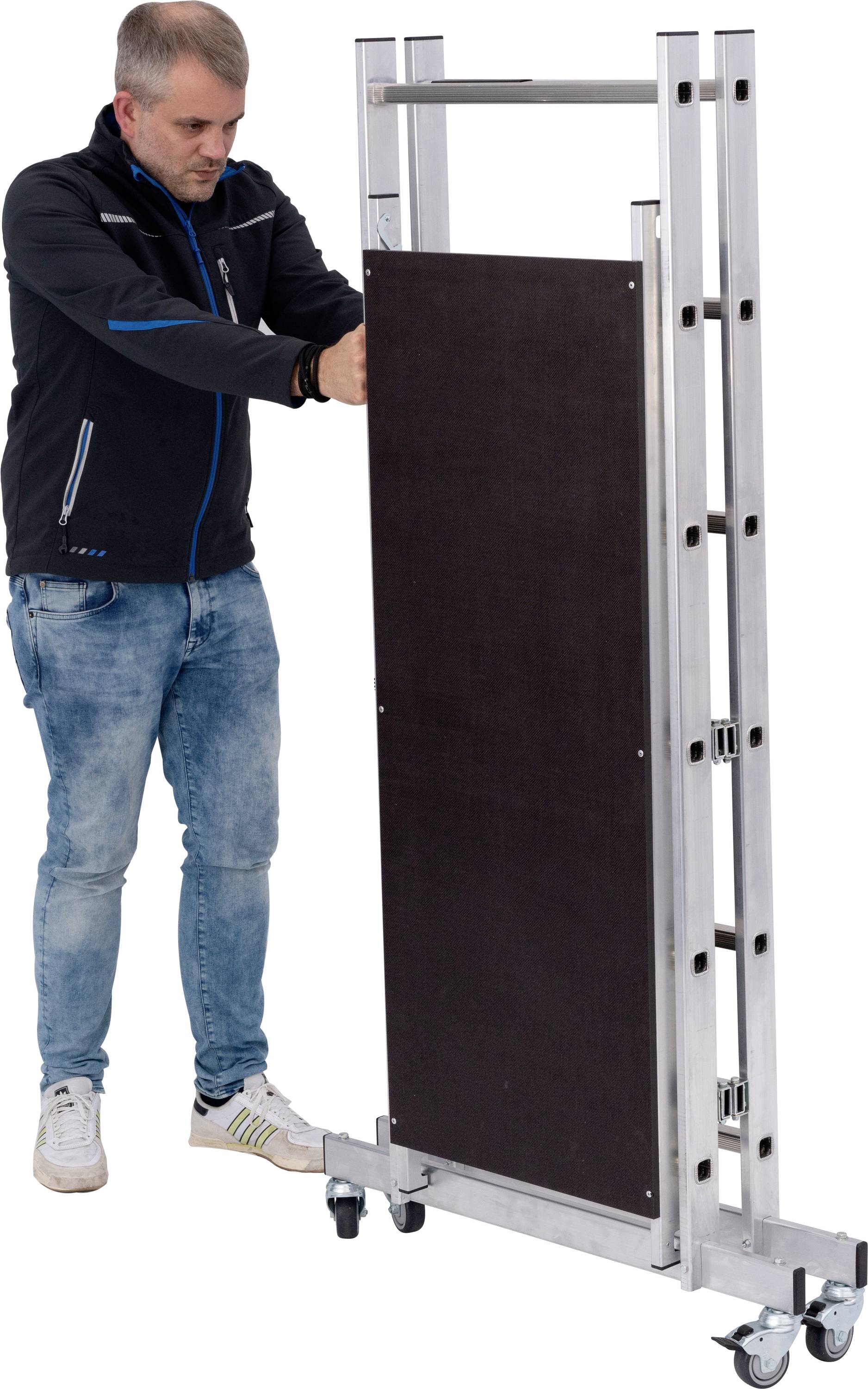 Muž v neformálnom oblečení posúva skladacie pódium na kolieskach, pravdepodobne za účelom prepravy alebo uskladnenia.