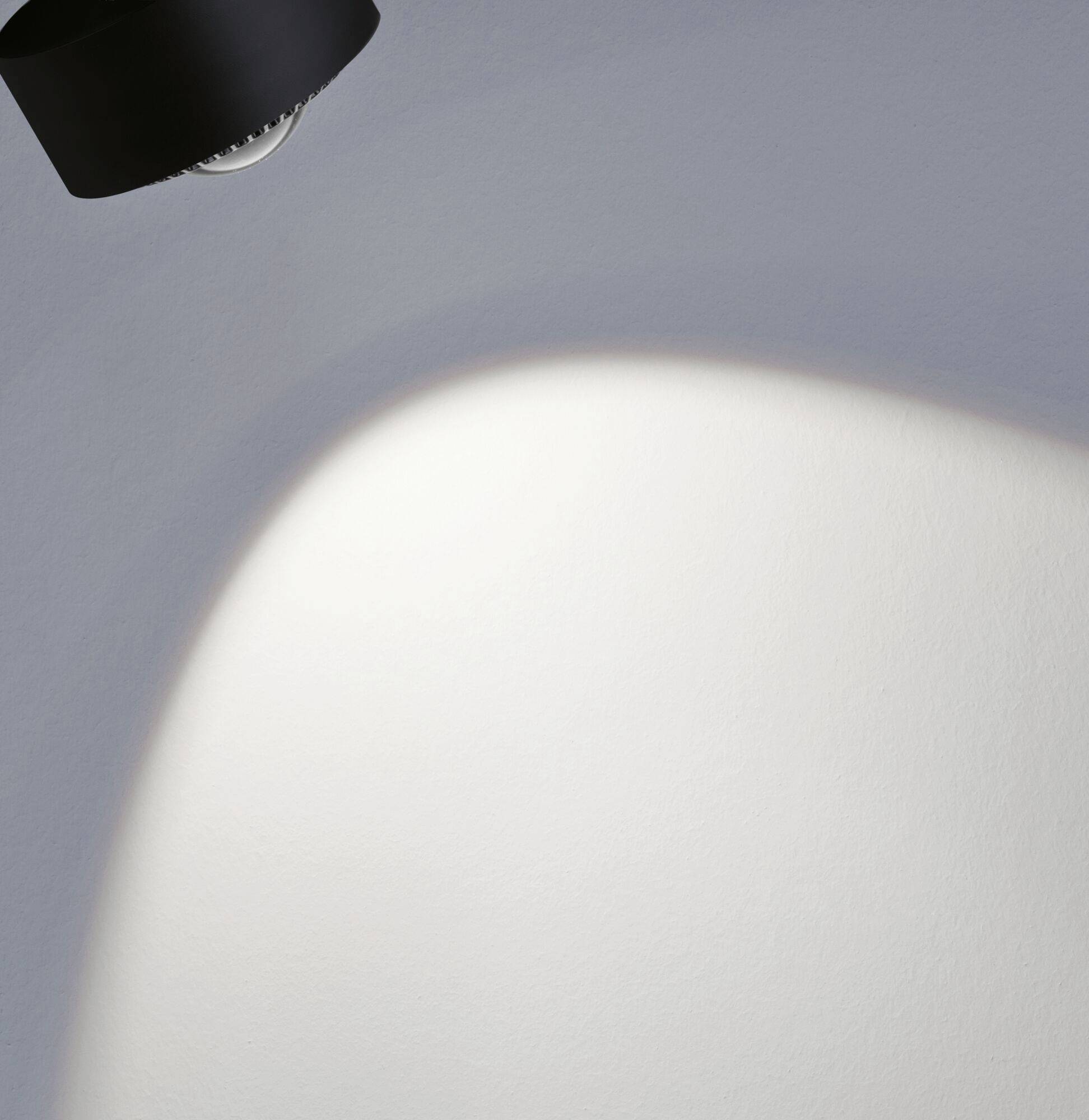 Lampa vrhá teplé svetlo na bielu zakrivená plochu a vytvára jemný prechod medzi svetlom a tieňom.