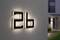 Číslo domu '26b' na stene, jemne osvetlené. V pozadí vstup a osvetlená cesta smerom k budove.