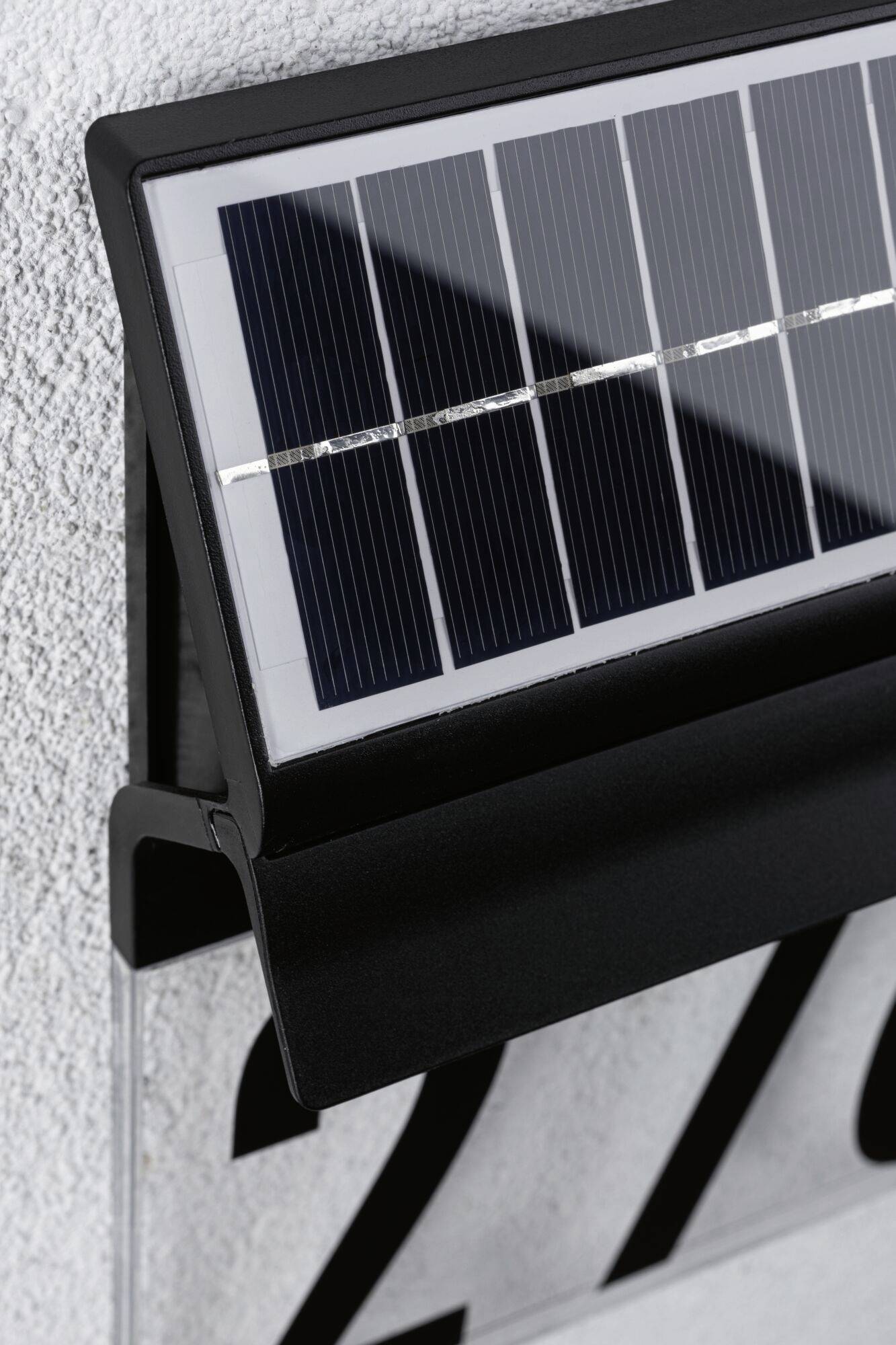 Solárna domová tabuľka s číslom domu namontovaná na stene, ktorá v tme osvetľuje číslo domu pre lepšiu viditeľnosť.