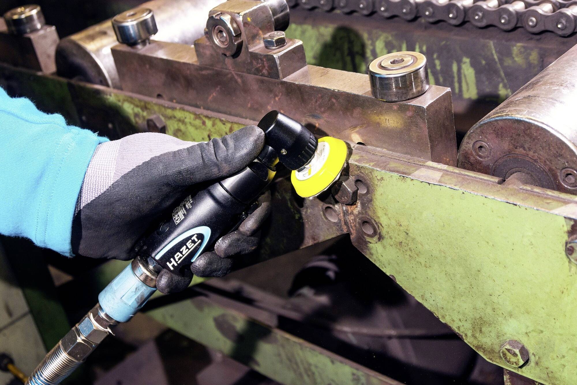 Osoba v pracovných rukaviciach drží elektrický nástroj, aby vyleštila kov na stroji. Prostredie pôsobí priemyselným dojmom.