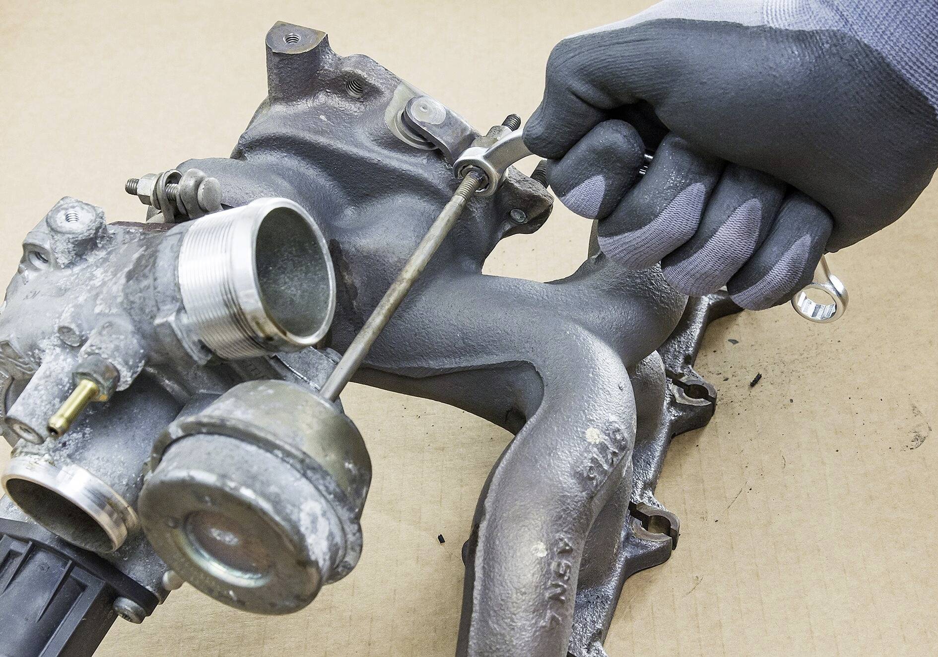 Rukavicou oblečená ruka opravuje turbodúchadlo pomocou skrutkovača. Pozadie je z kartónu.