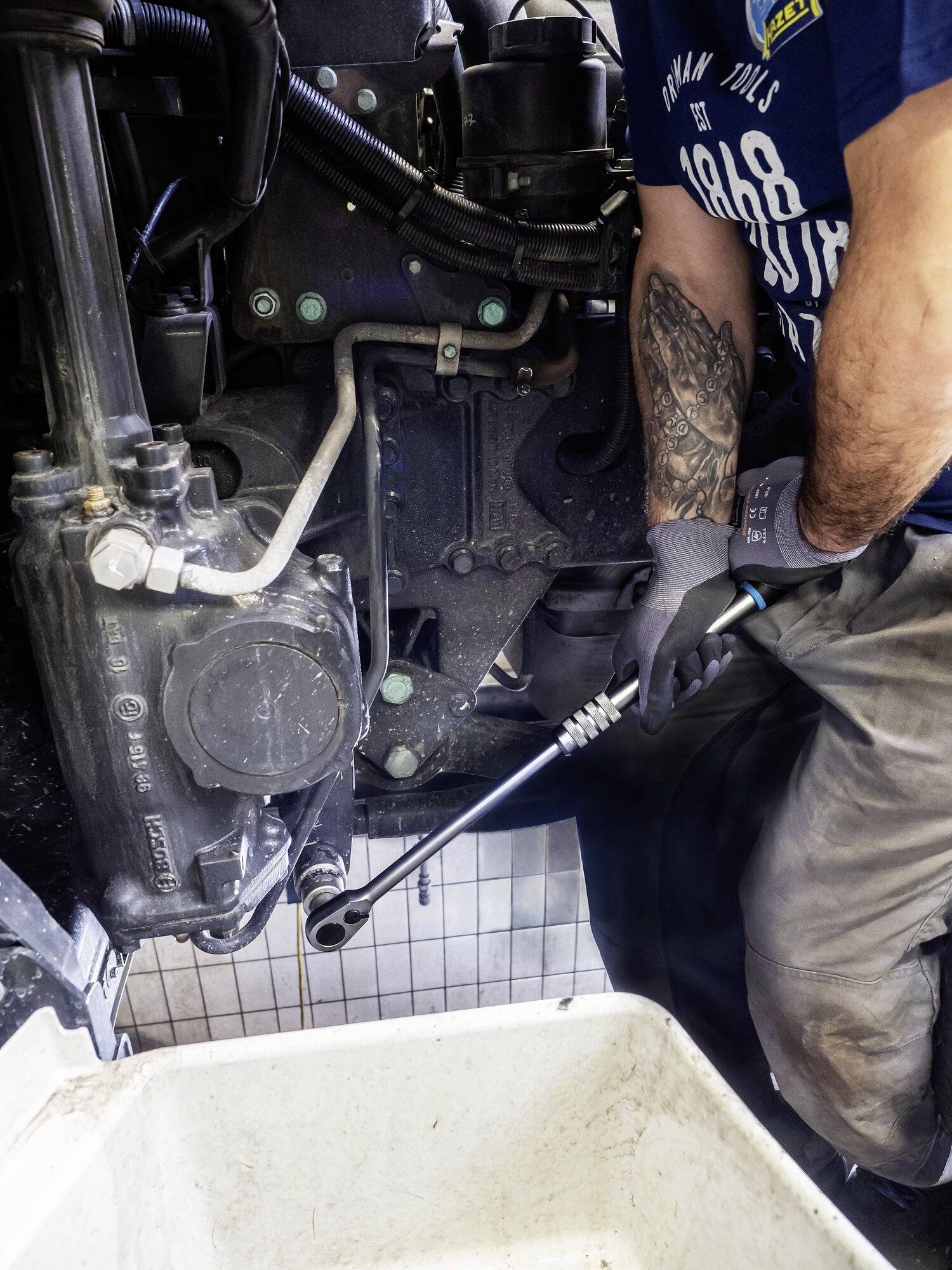 Osoba opravuje motor, drží nástroj v ruke. Dôraz je kladený na technickú prácu so zobraziteľnými strojovými súčiastkami.