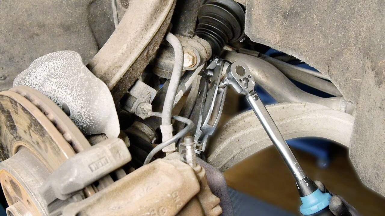 Mechanik uťahuje skrutku v podvozku automobilu pomocou račňového kľúča. Prostredie je špinavé a prašné.