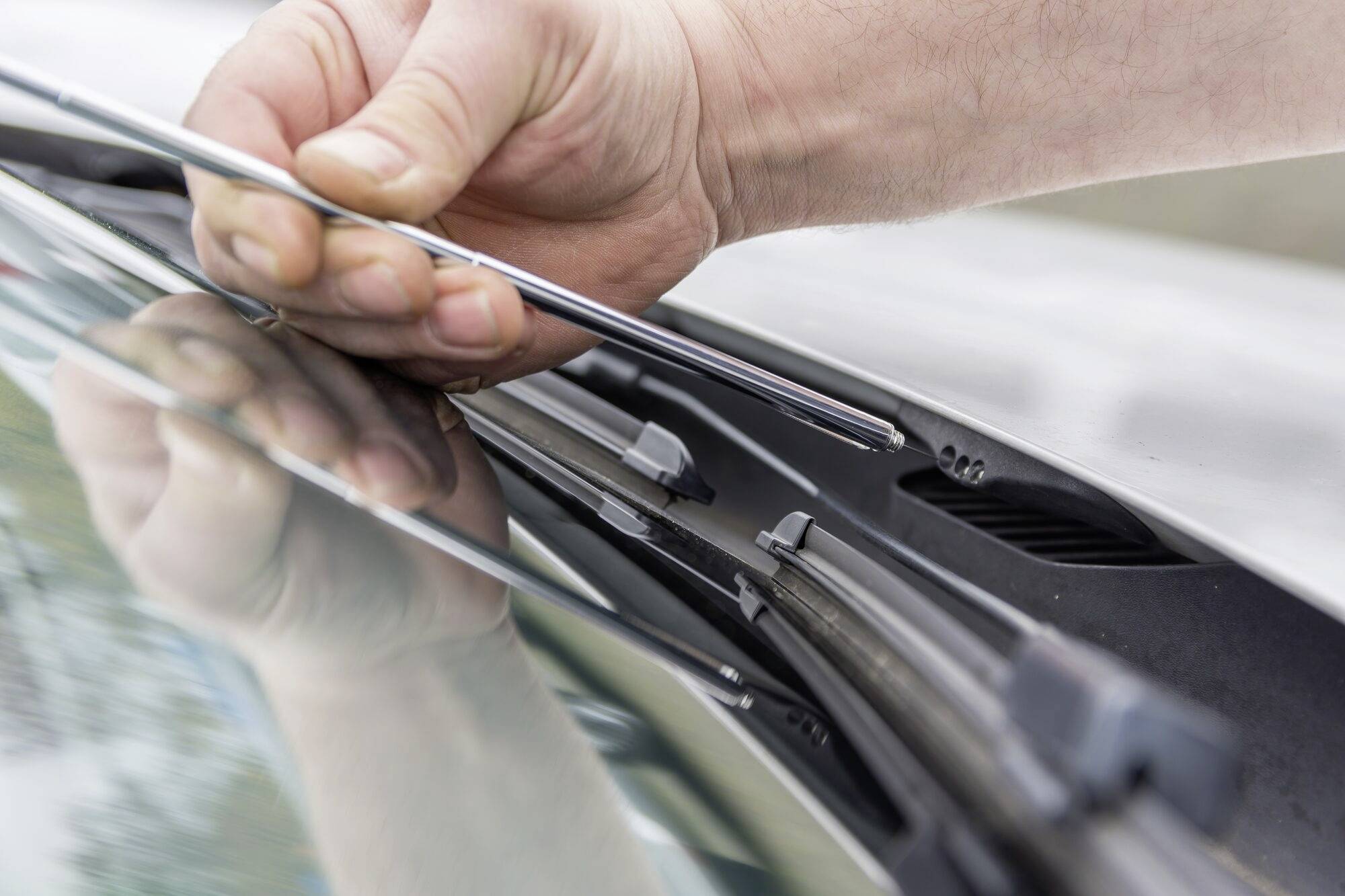 Ruka vymieňa stierač na automobile. Detailný záber zachytáva nasadzovanie stieracej lišty do držiaka.