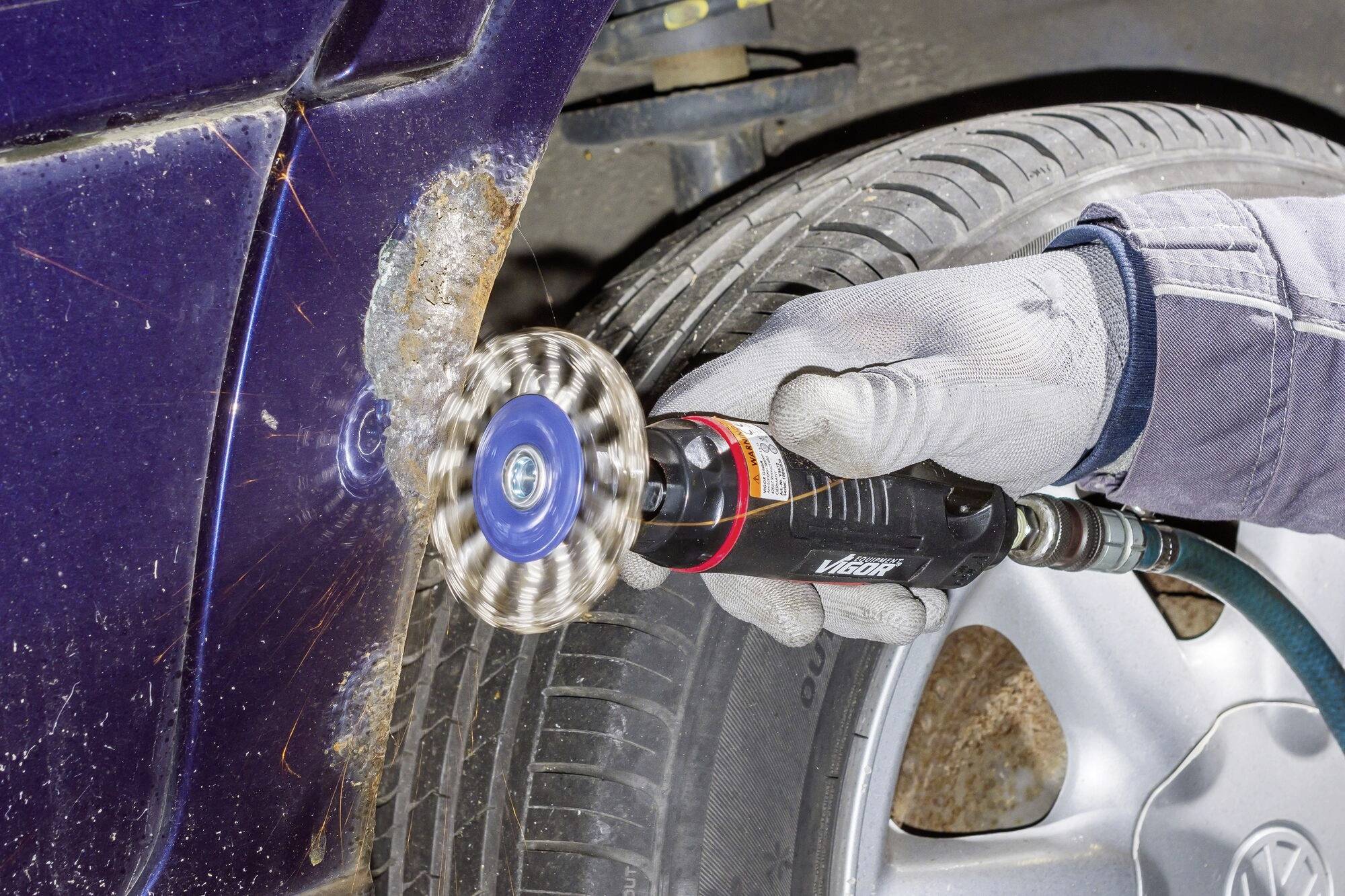 Mechanik brúsi hrdzu z pneumatiky automobilu elektrickou brúskou. Pri práci z nej strieľajú iskry.