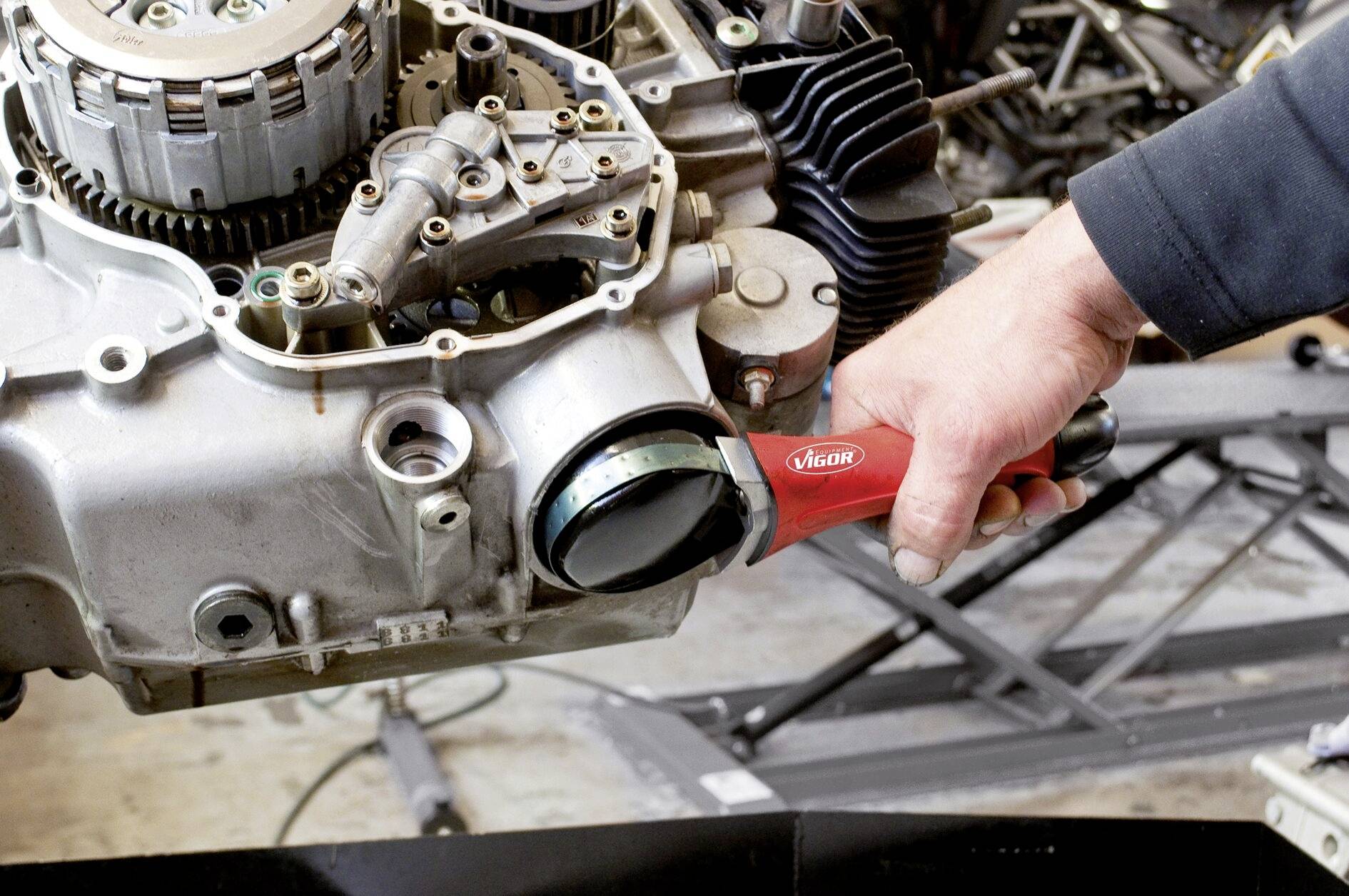 Osoba odstraňuje červeným náradím olejové sitko z motorového bloku motocykla v prostredí dielne.