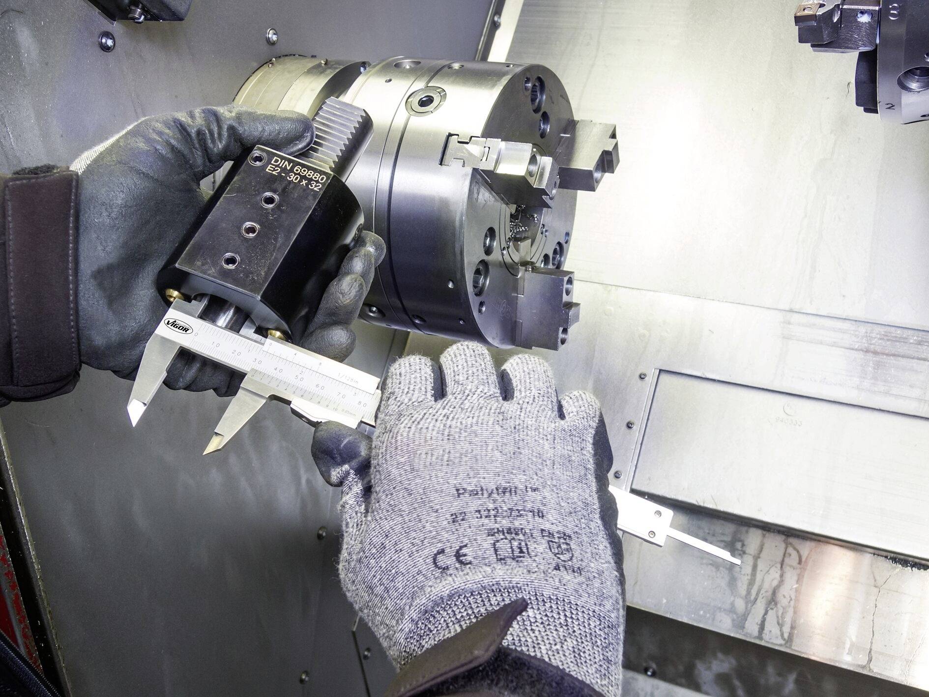 Pracovník meria obrobok na sústruhu pomocou digitálneho posuvného meradla.