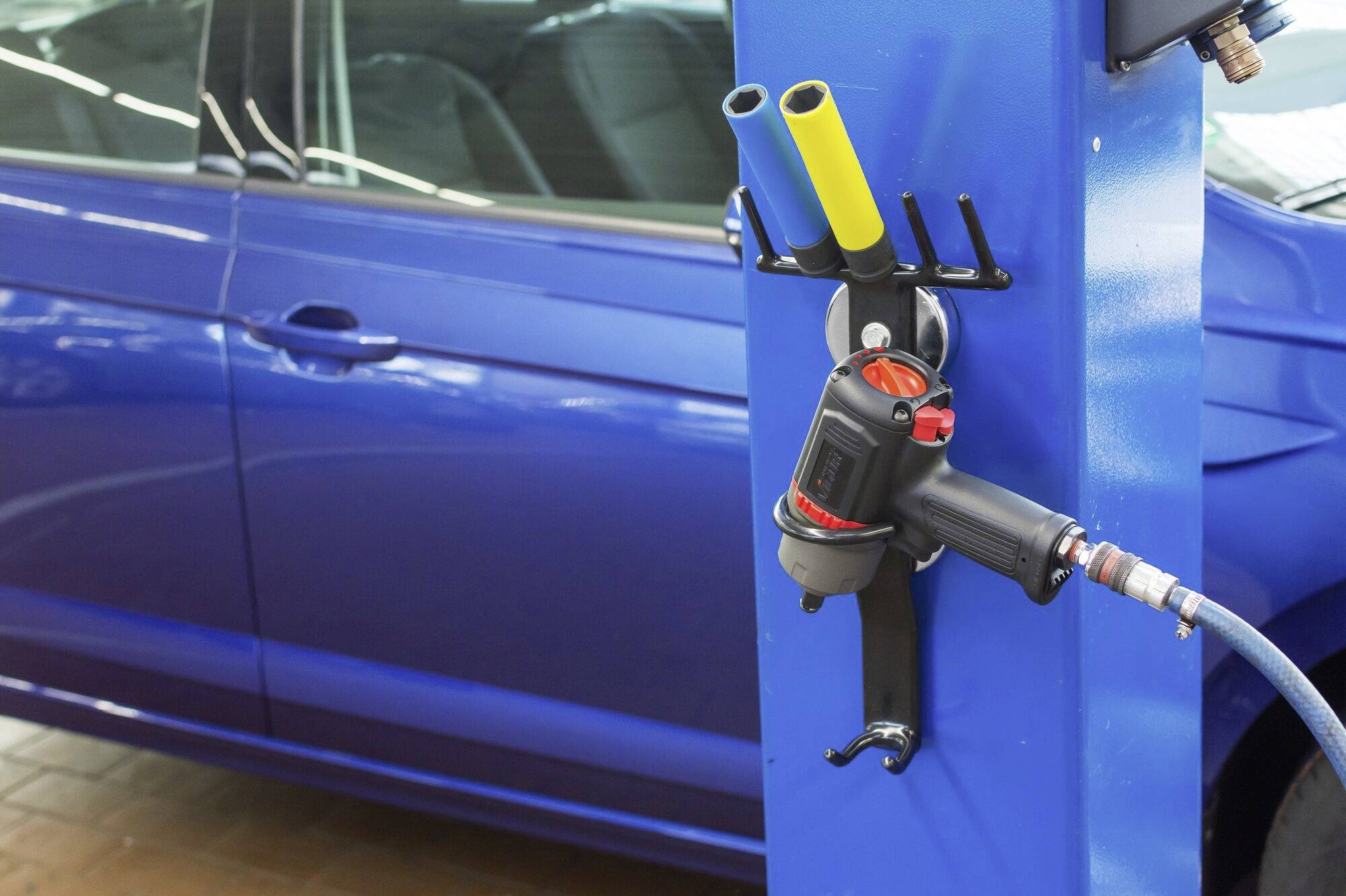 Modrý automobil stojí vedľa vzduchovej pištole, ktorá visí pri modrej čerpacej stanici.