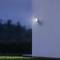 Vonkajšia lampa svieti na stene za súmraku alebo v noci. V pozadí je viditeľná rozmazaná, tmavá krajina.