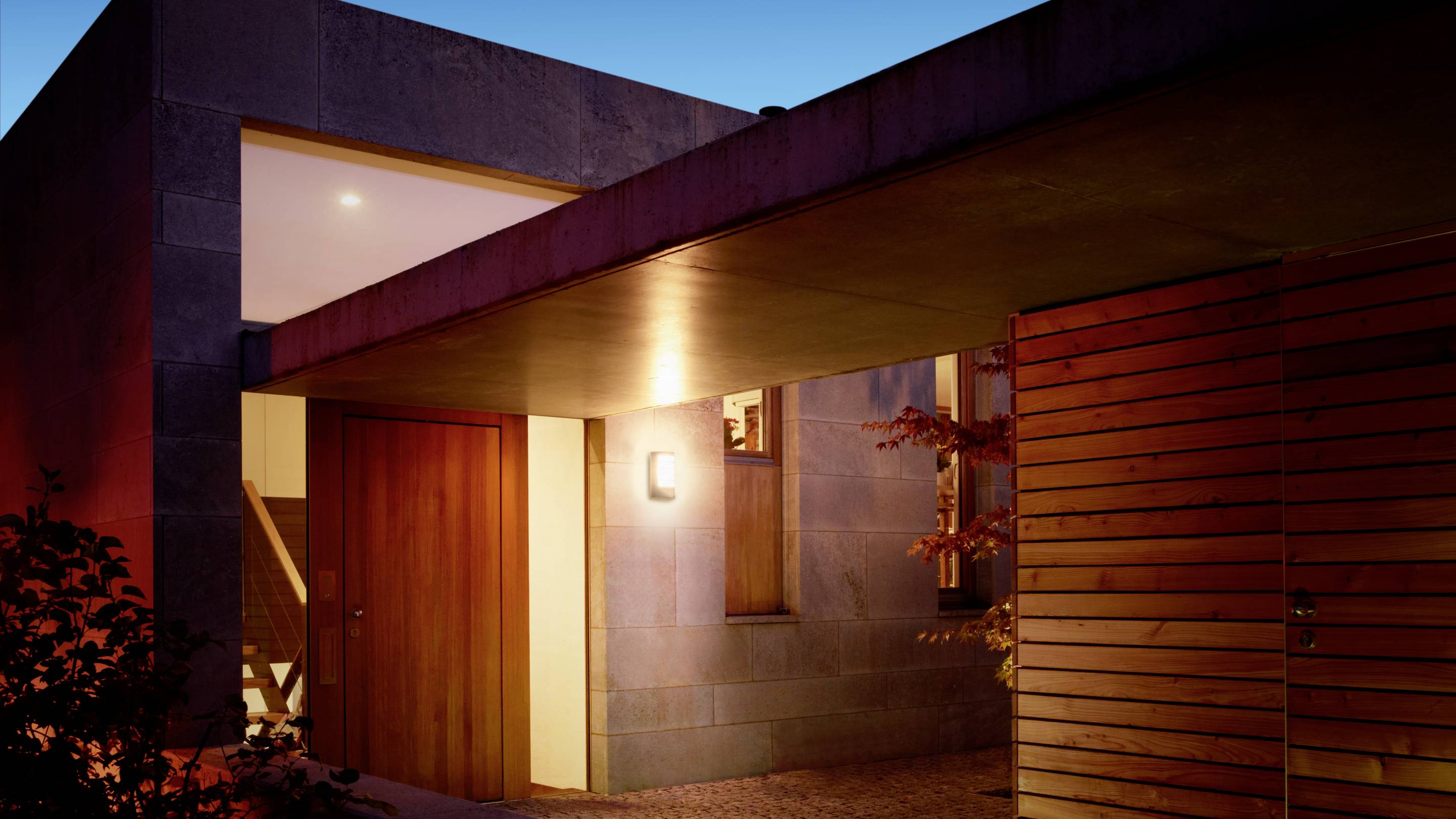 Moderný dom v noci, osvetlený vonkajšími svetlami. Drevo a kameň dominujú architektonickému stvárneniu.