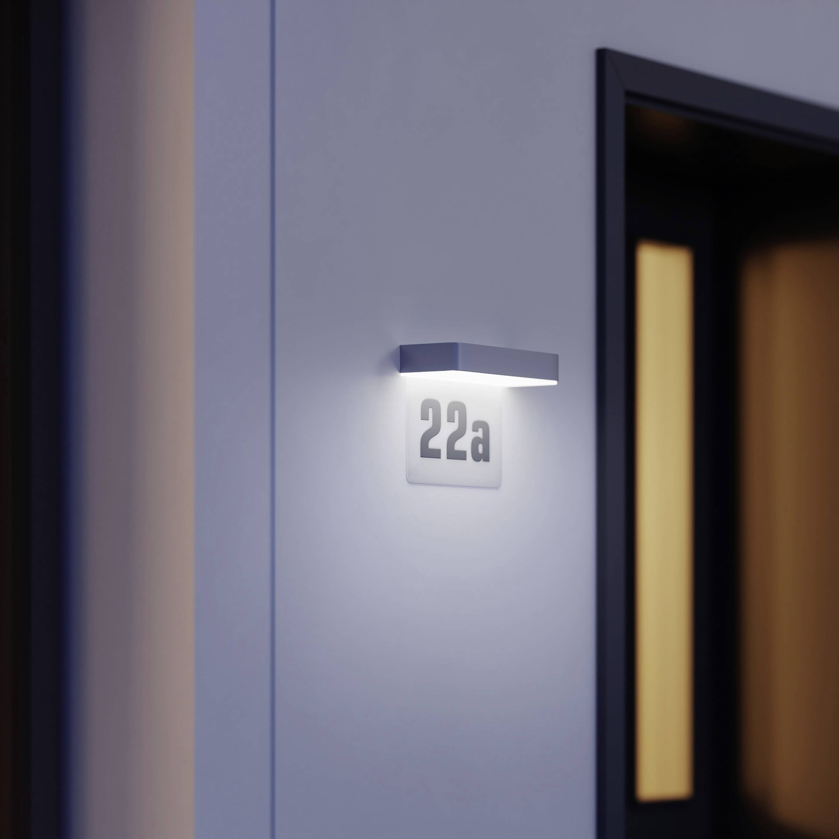 Chodba s dverami, nad ktorými je cedula s nápisom '22a', osvetlená moderným nástenným svietidlom.