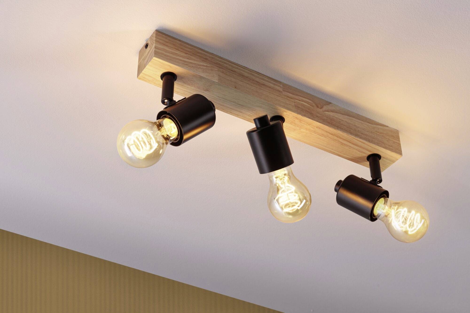 Trojplameňový stropný luster so žiarovkami a dreveným držiakom, namontovaný na strope a smerujúci do priestoru.