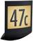 Osvetlená tabuľka na stene s číslom '47c' v čiernom písme na žltom pozadí.