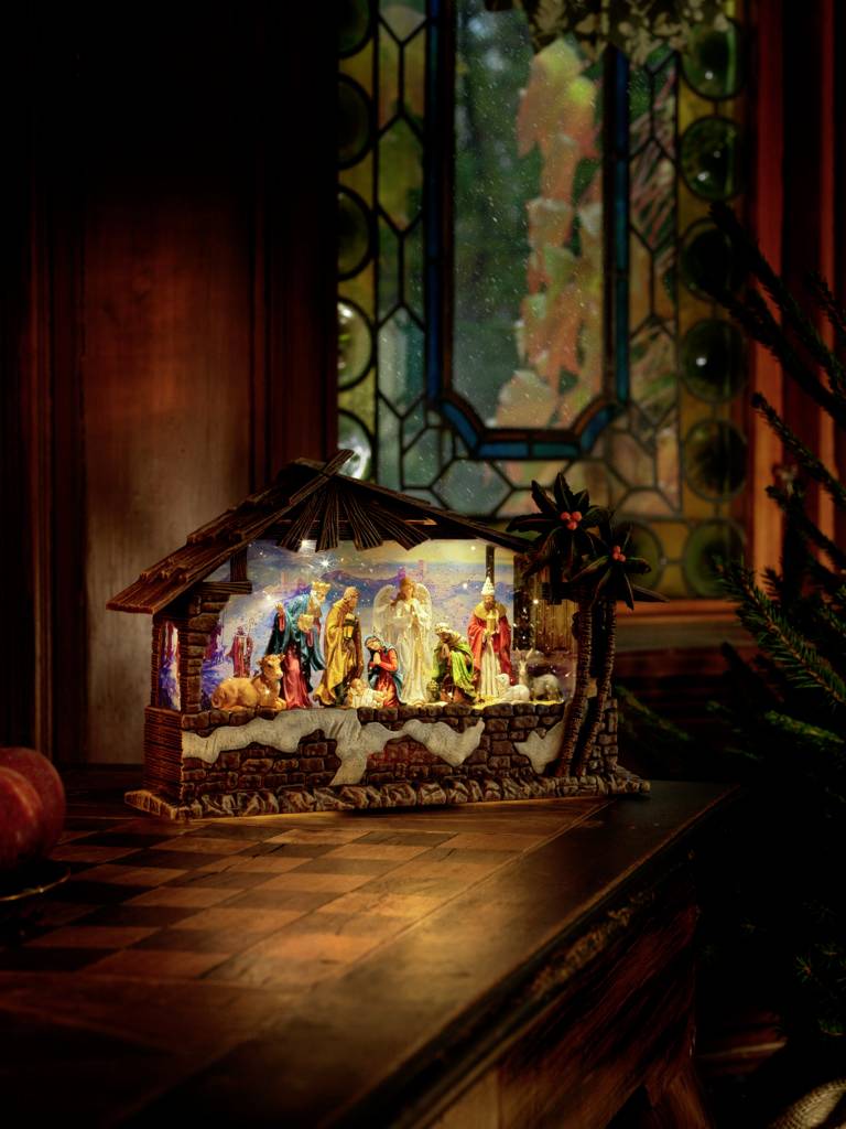 Výjav betlehemskej scény s postavami v drevenom maštali pred farebným kostolným vitrážovým oknom; zobrazenie Ježišovho narodenia.