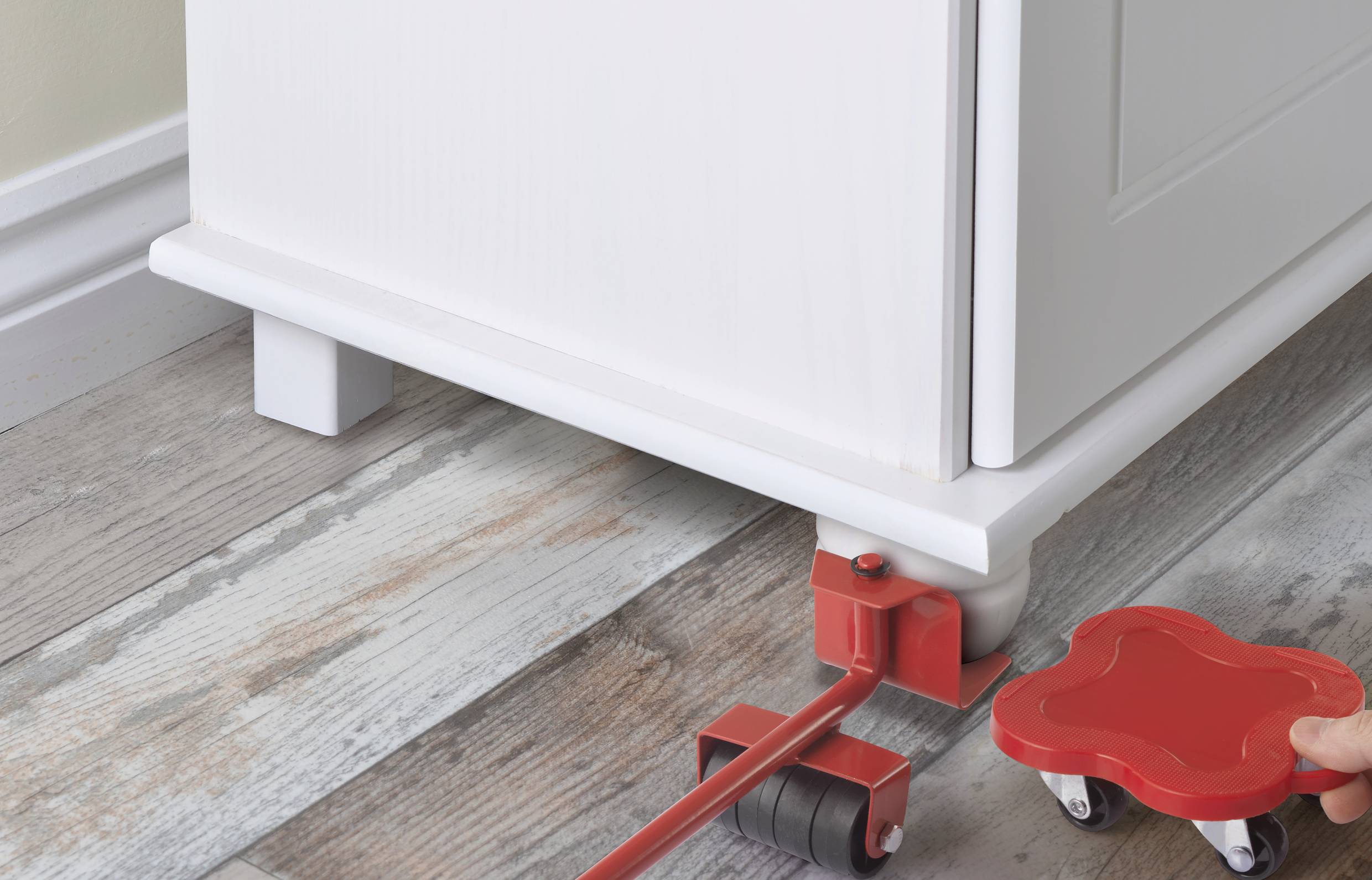 Osoba presúva kus nábytku červeným nábytkovým výťahom po drevnej podlahe.
