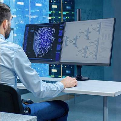 Osoba pracuje na počítači s dvoma monitormi a analyzuje dáta pred pozadím so servermi.