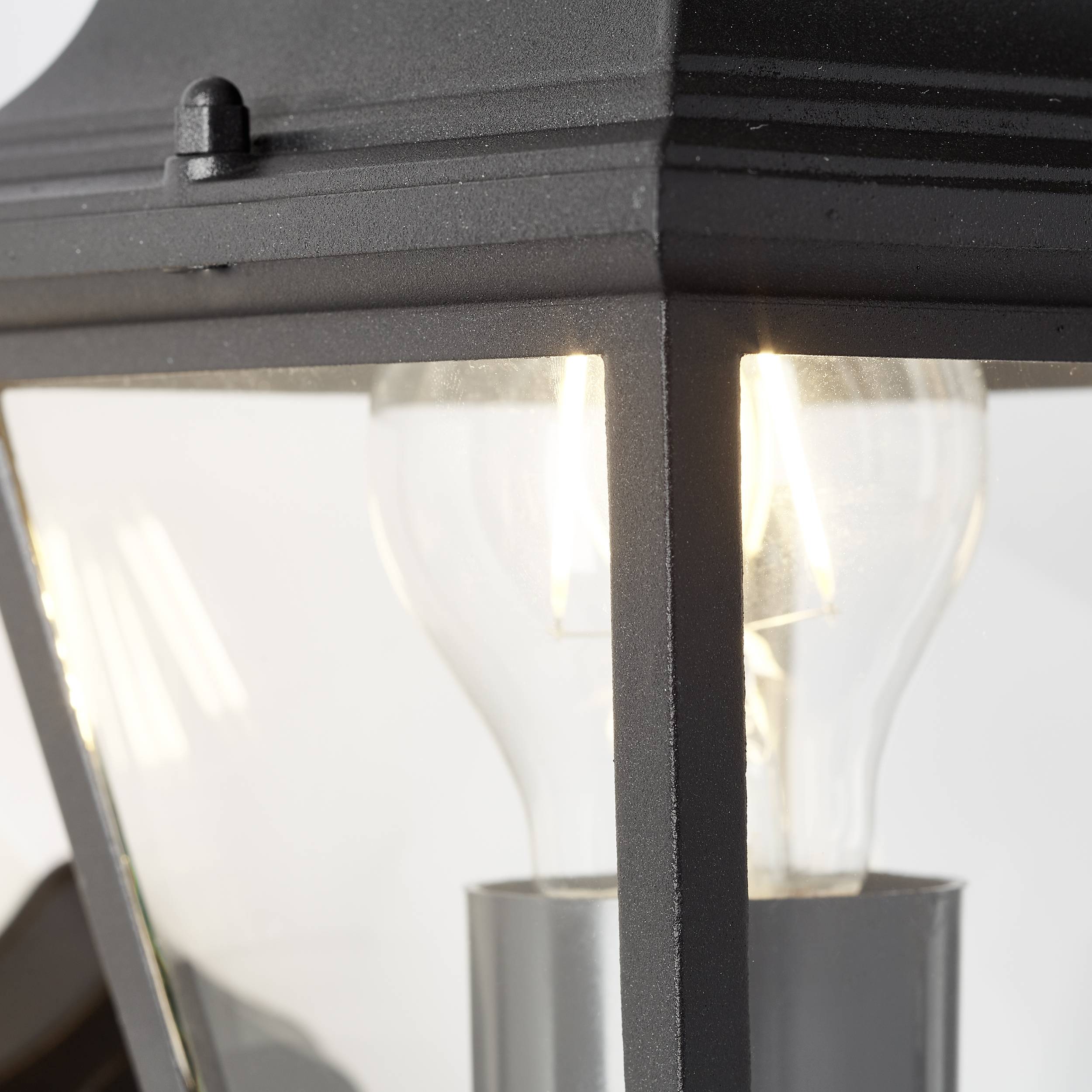 Detailný záber pouličnej lampy so sklenenými stenami a jasne svietiacou žiarovkou vnútri, ktorá vyžaruje teplé svetlo.