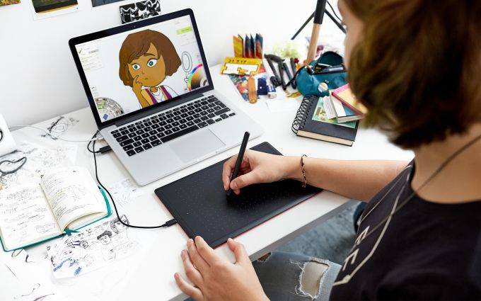 Osoba kreslí na grafickom tablete a pozerá sa na návrh kreslenskej postavy na obrazovke laptopa.