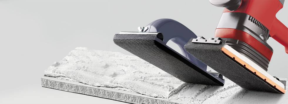 Červená brúska opracováva biely, zvlnený povrch, zatiaľ čo druhé brúsne zariadenie zaujíma pozíciu vedľa nej.