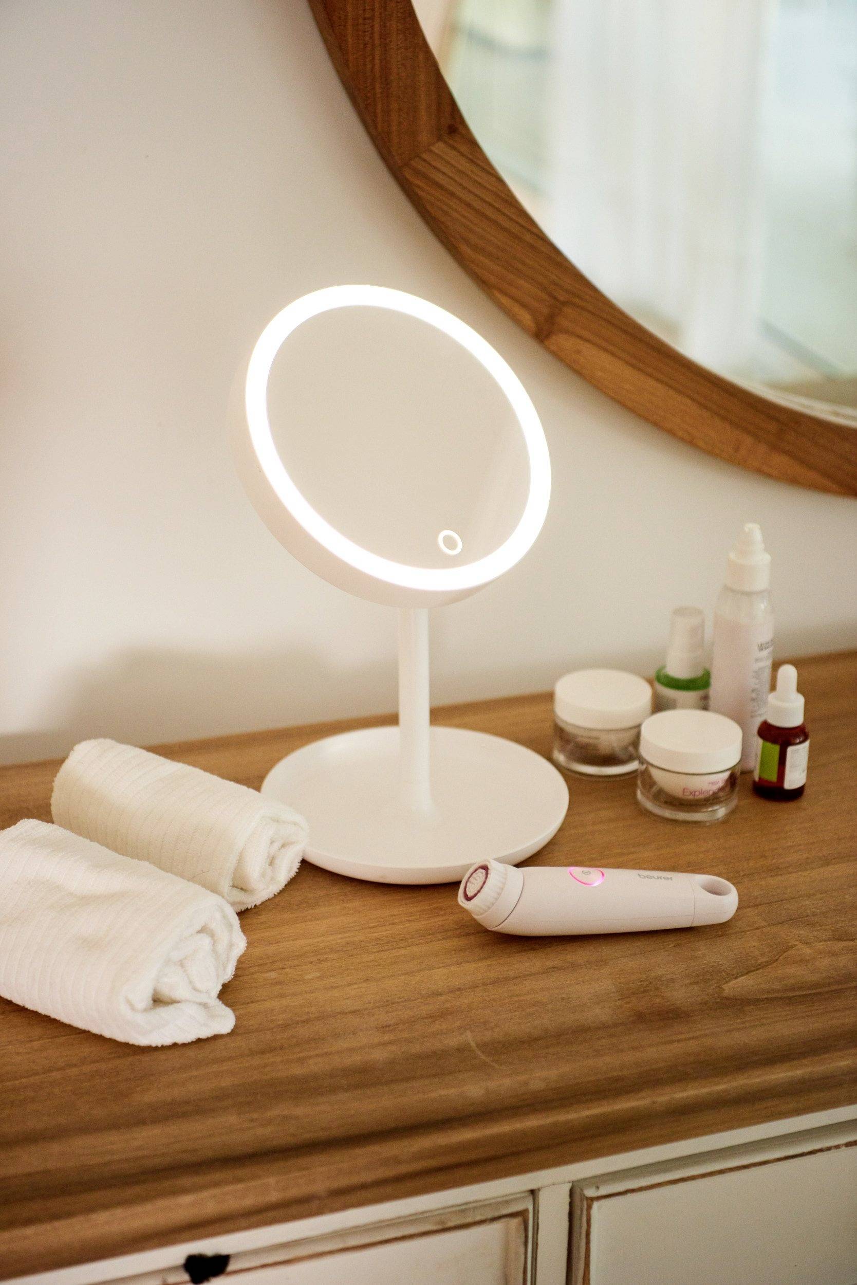 Kozmetický stolík s osvetleným make-up zrkadlom, uterákmi a ošetrujúcimi produktmi.