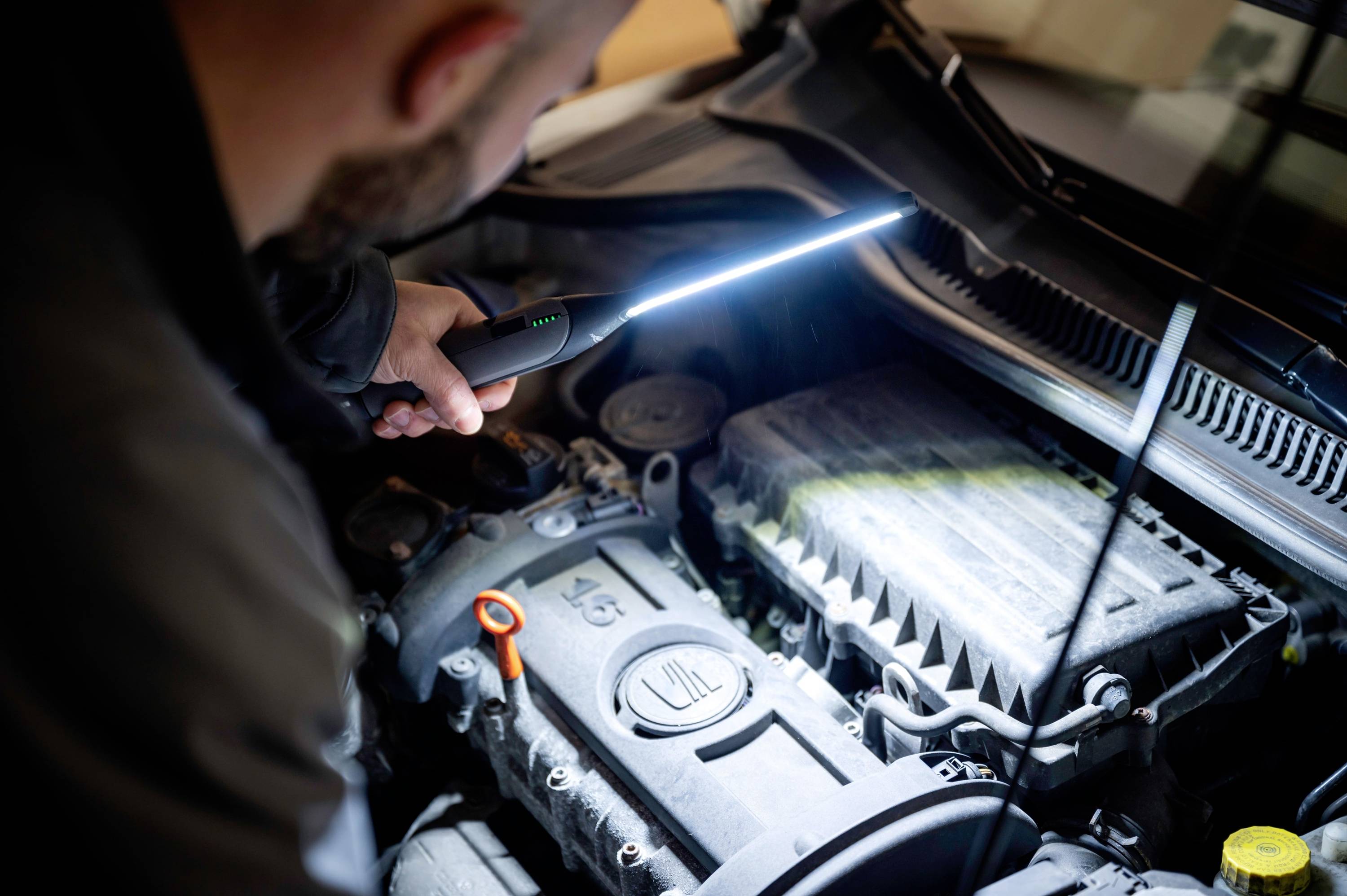 Mechanik skúma motor auta vreckovou lampou. Tiene a svetlo zvýrazňujú štruktúry motora.