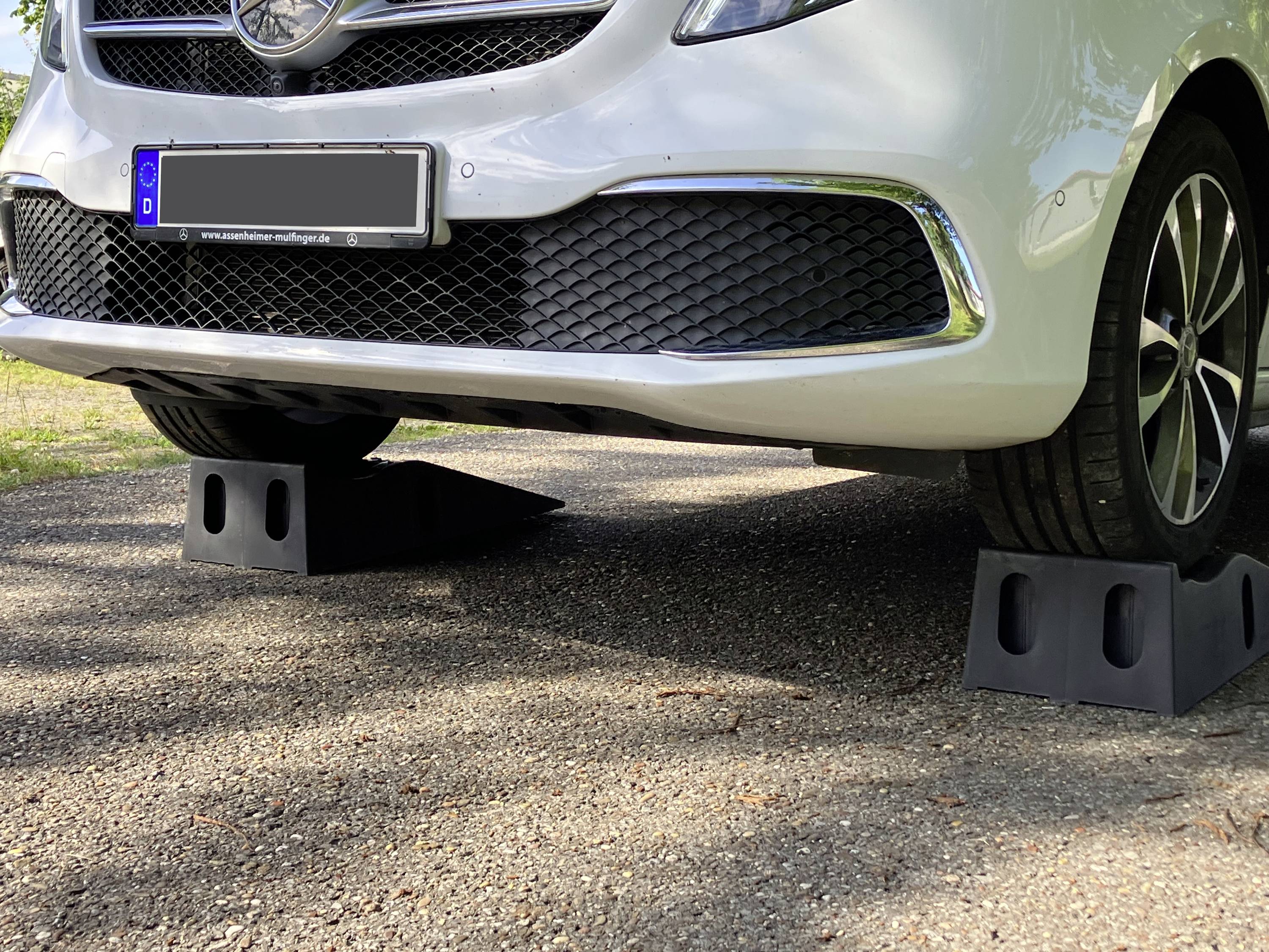 Biele auto stojace na dvoch čiernych zdvíhacích plošinách na zdvihnutie prednej časti. Spodná predná nárazníková časť a predné kolesá sú viditeľné.