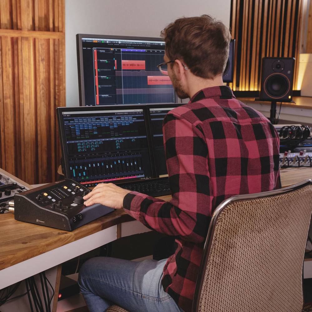 Osoba s nasadenými slúchadlami pracuje na počítači s audiopostprodukčným softvérom v nahrávacom štúdiu.