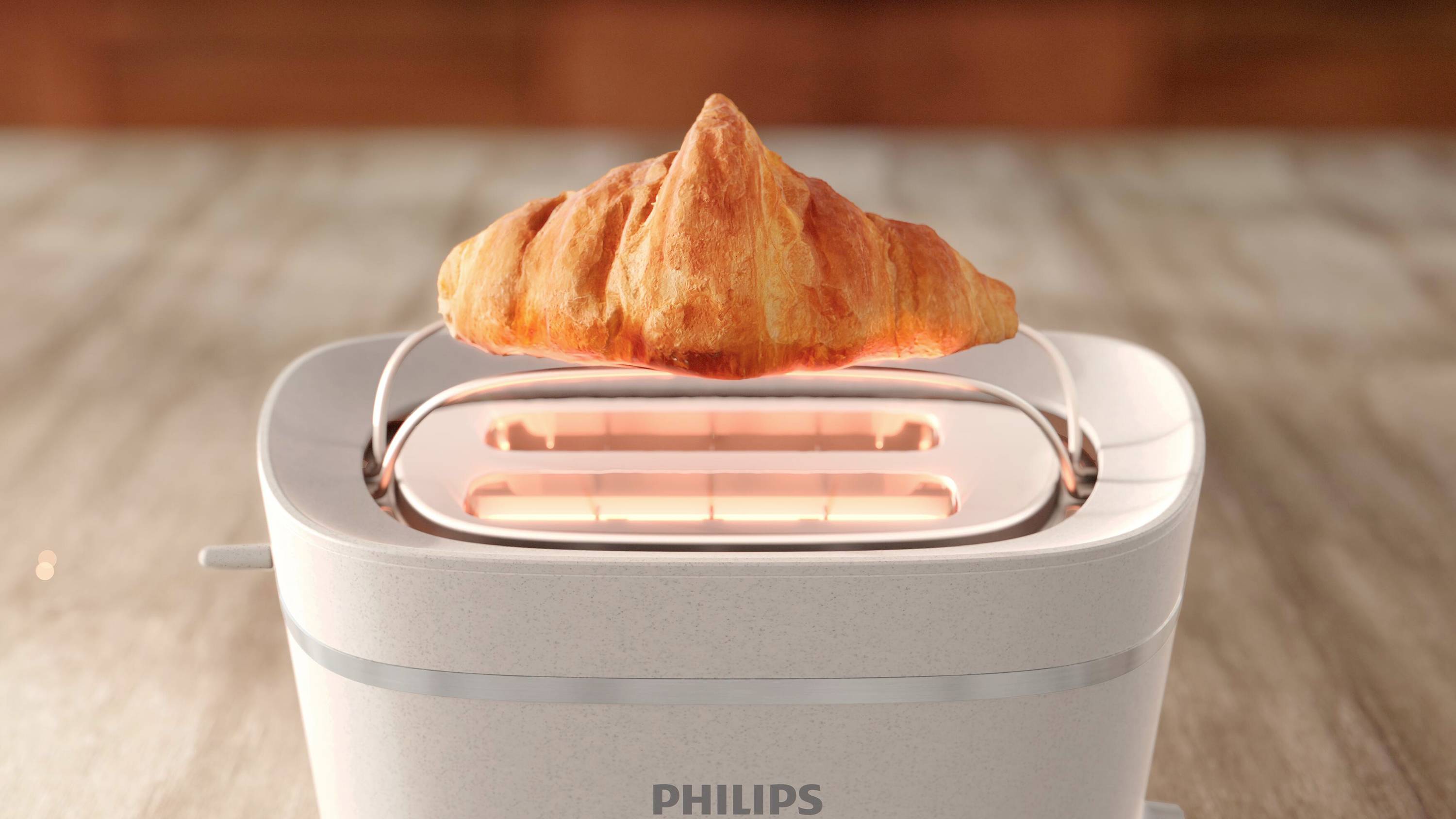 Zlatohnedý croissant sa opečie v toasteri značky Philips. Toaster stojí na kuchynskej pracovnej doske.