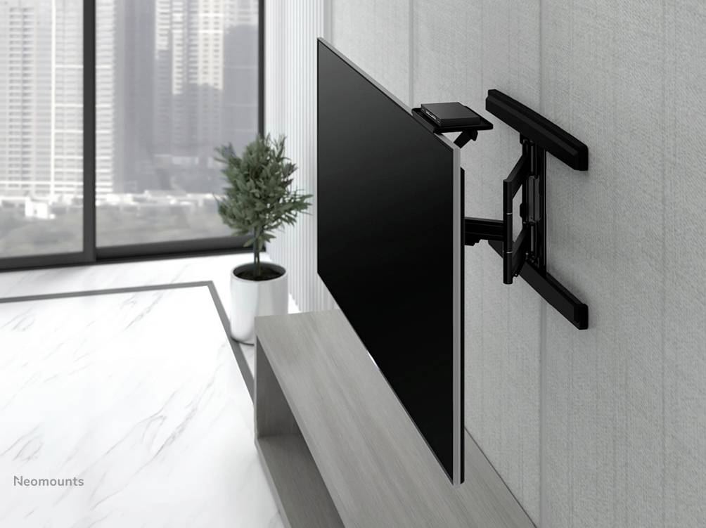 Plochý televízor je upevnený na otočnom držiaku na stene. V pozadí sú veľké okná s výhľadom na mesto.