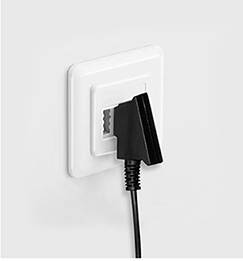 Čierny konektor je zasunutý do bielej elektrickej zásuvky na stene.