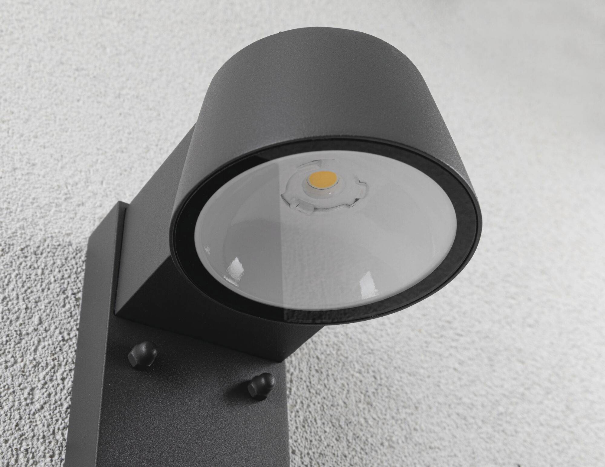 Čierna nástenná lampa je namontovaná na sivej stene. Má moderný dizajn s okrúhlym tienidlom a LED svetelným zdrojom.