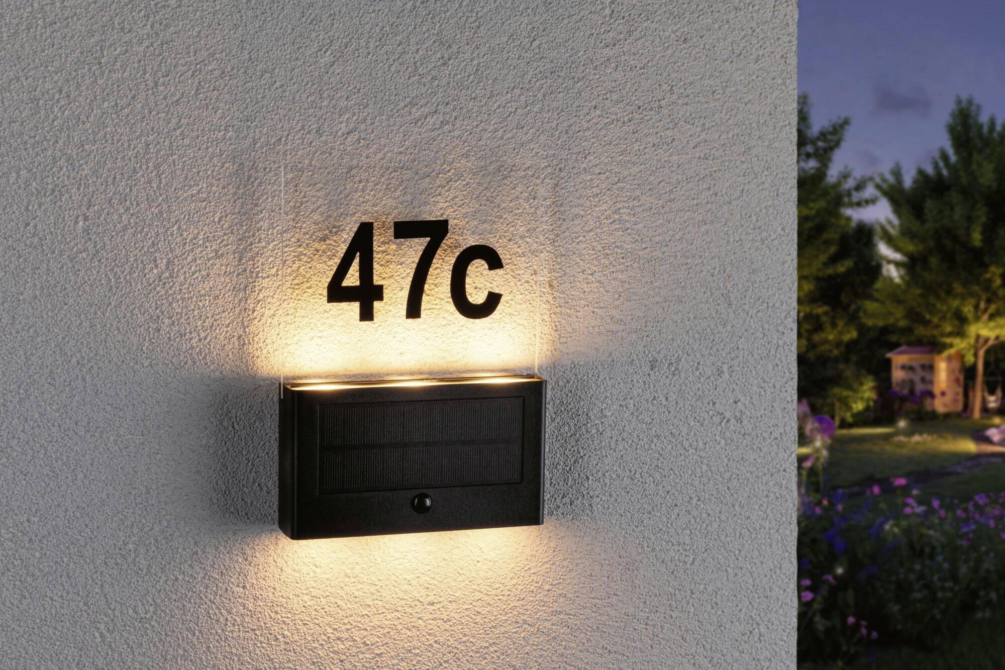 Osvetlené číslo domu '47c' na stene za súmraku, obklopené záhradou a stromami.