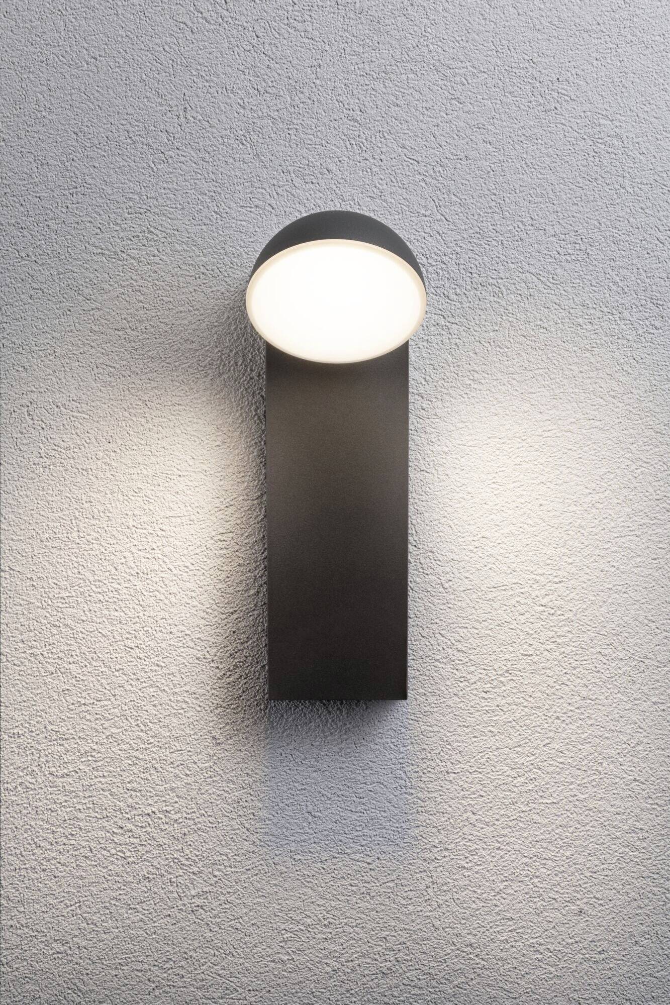 Moderná nástenná lampa v čiernej farbe, rovnomerne osvetľuje sivú stenu.