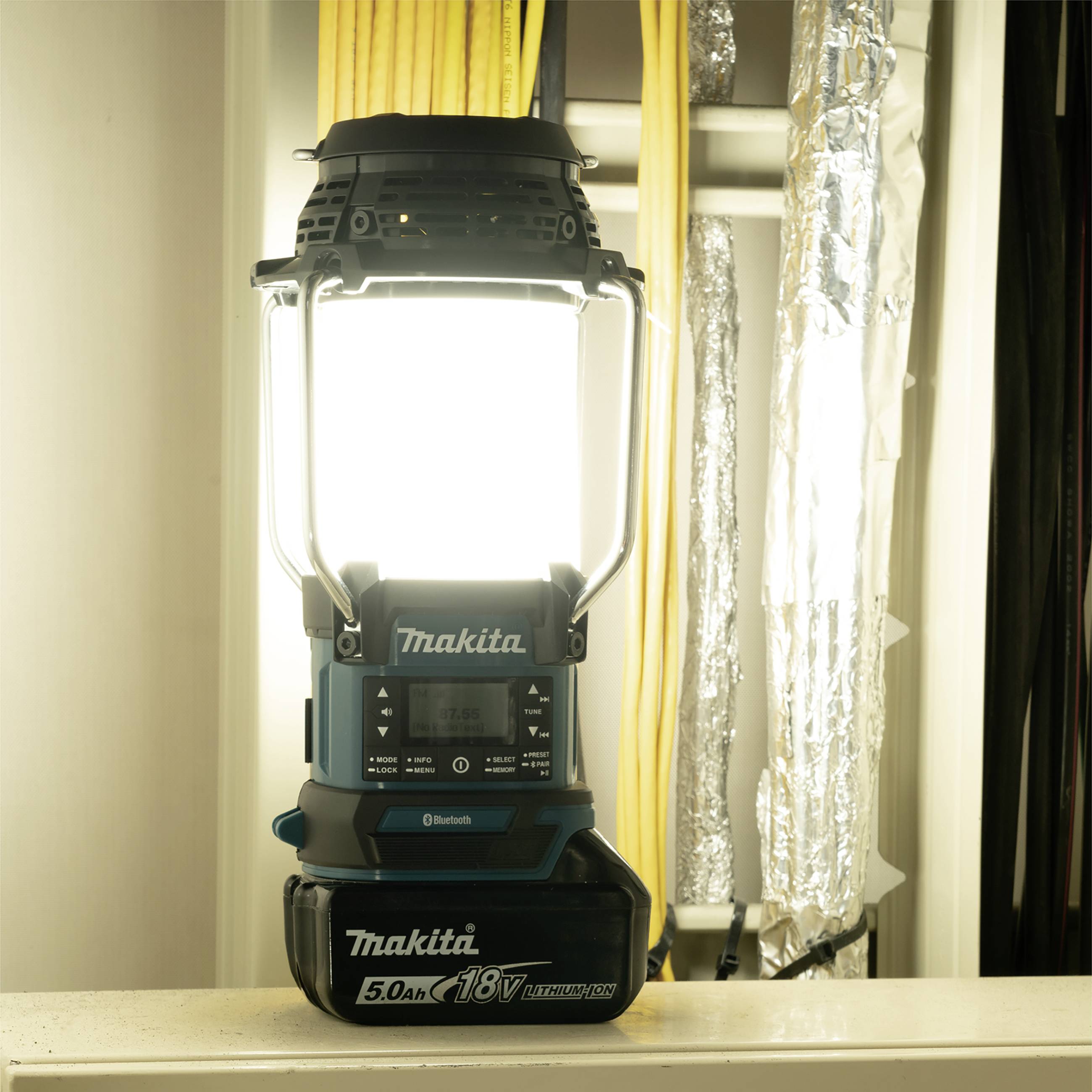 Jasná pracovná lampa stojí v miestnosti, obklopená káblami a potrubiami. Vyžaruje silné svetlo a osvetľuje priestor okolo seba.
