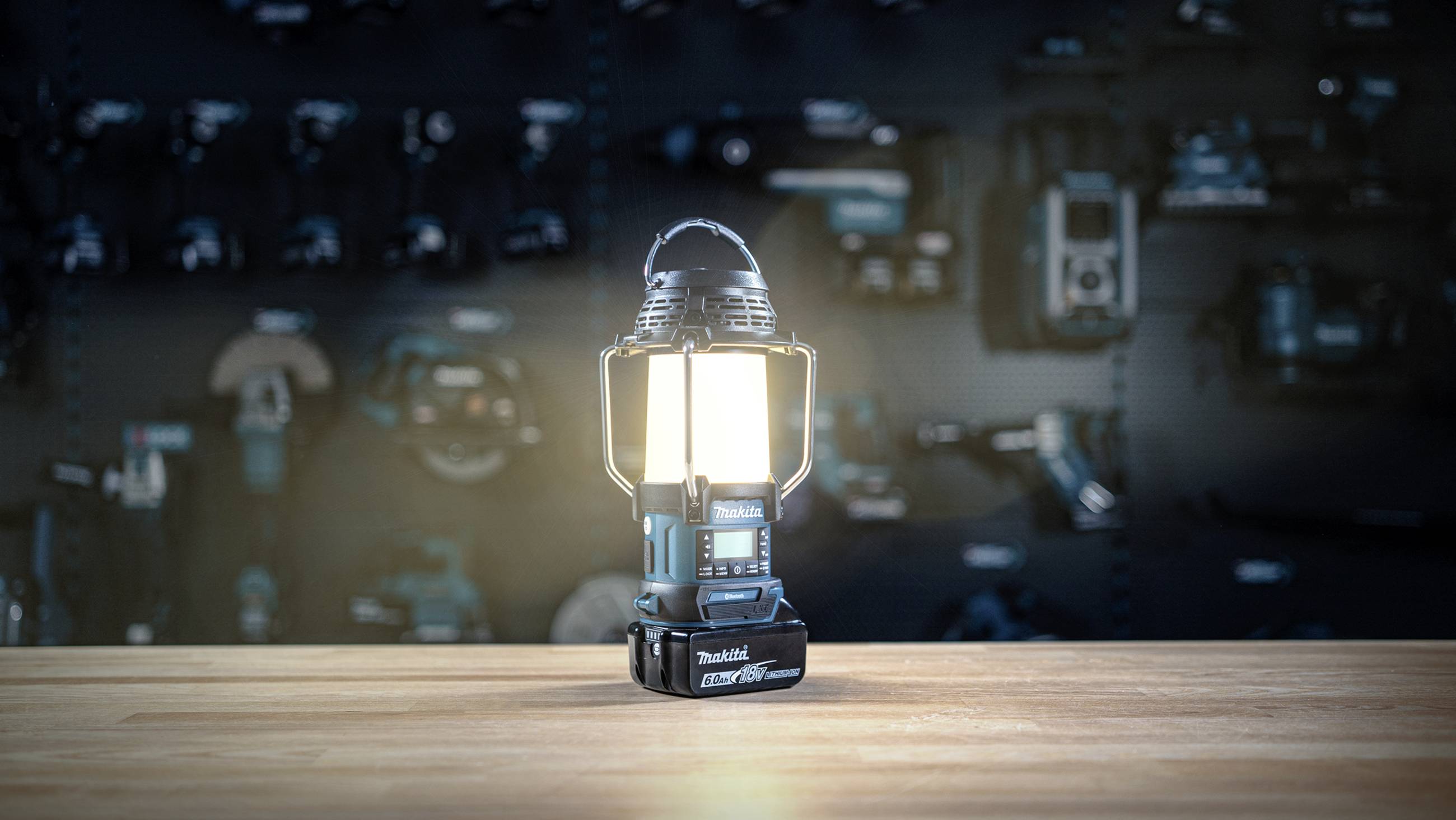 Elektrická pracovná lampa na drevenej doske pred pozadím nástrojov. Lampa je zapnutá a svieti jasným svetlom.