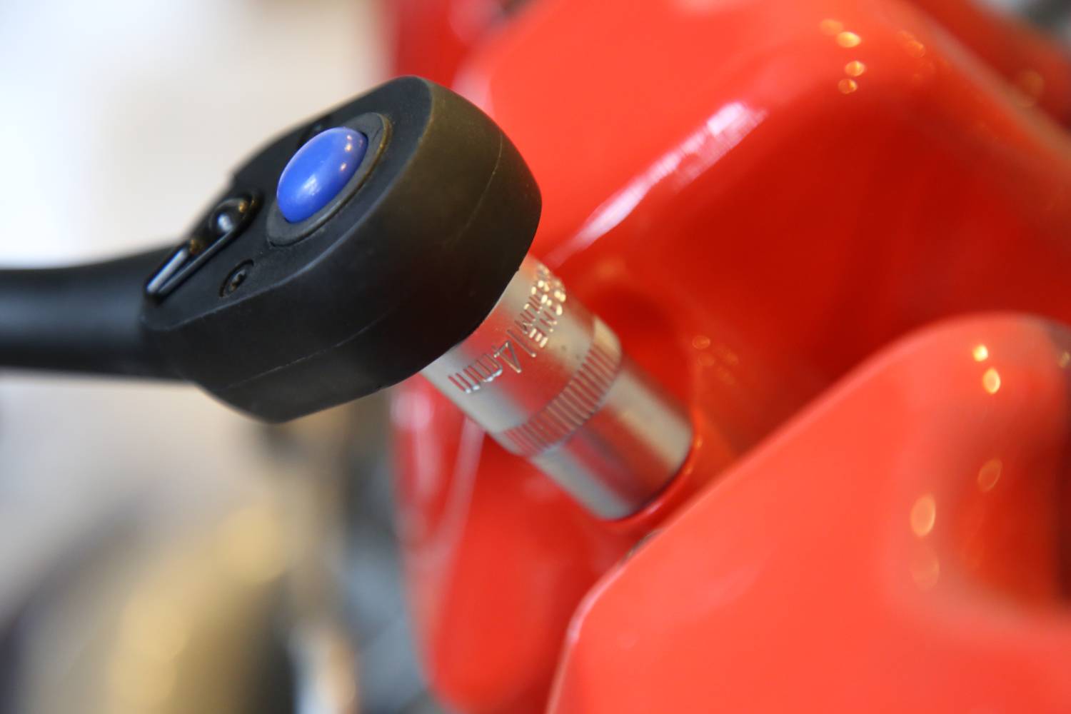 Detailný záber kľúča, ktorý pracuje na červenom povrchu, pravdepodobne ako súčasť motorového mechanizmu.