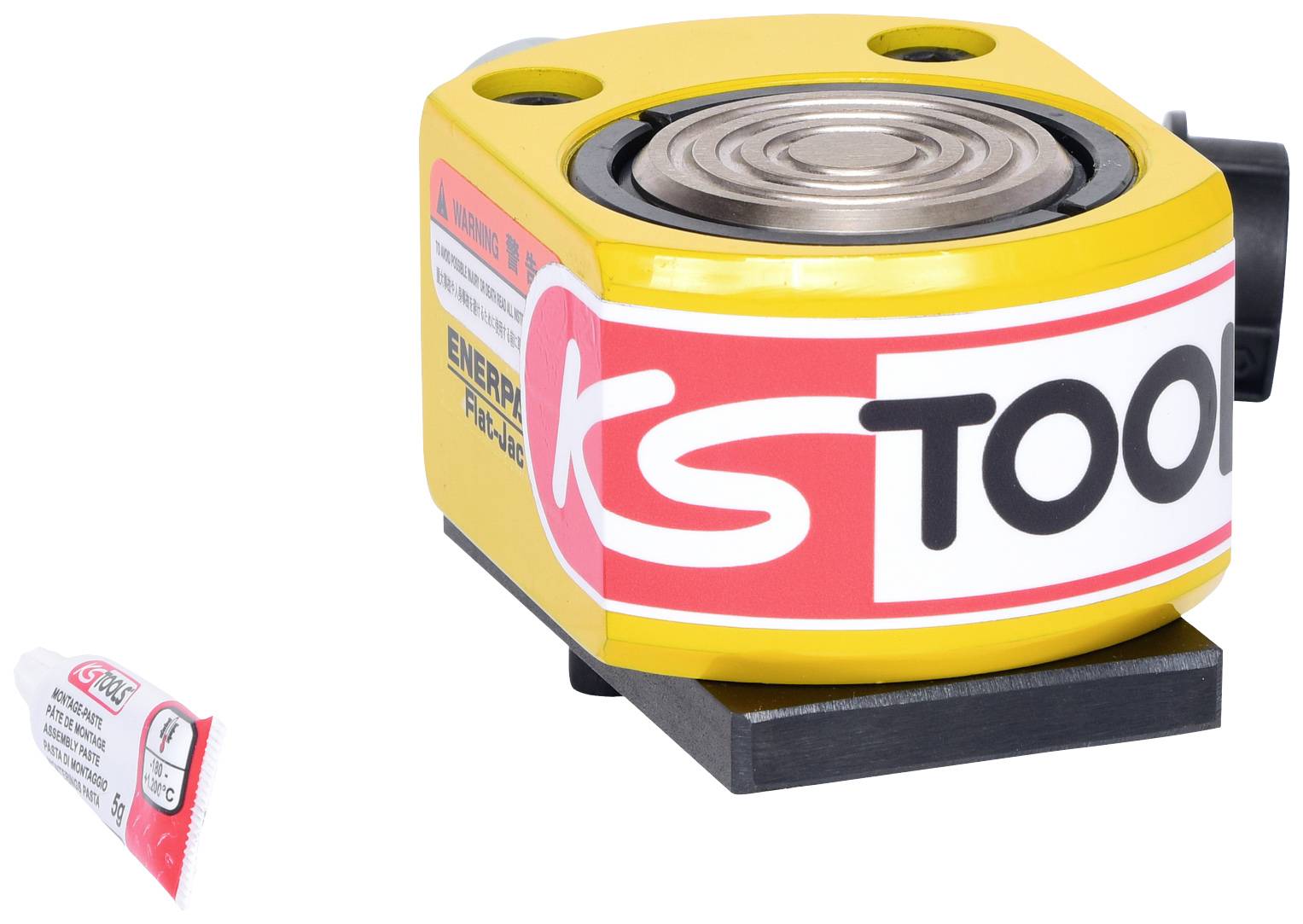 Hydraulický valec v žltom puzdre s logom 'KS TOOLS' napravo, na čiernej základni. Na ľavej strane malá tuba maziva.