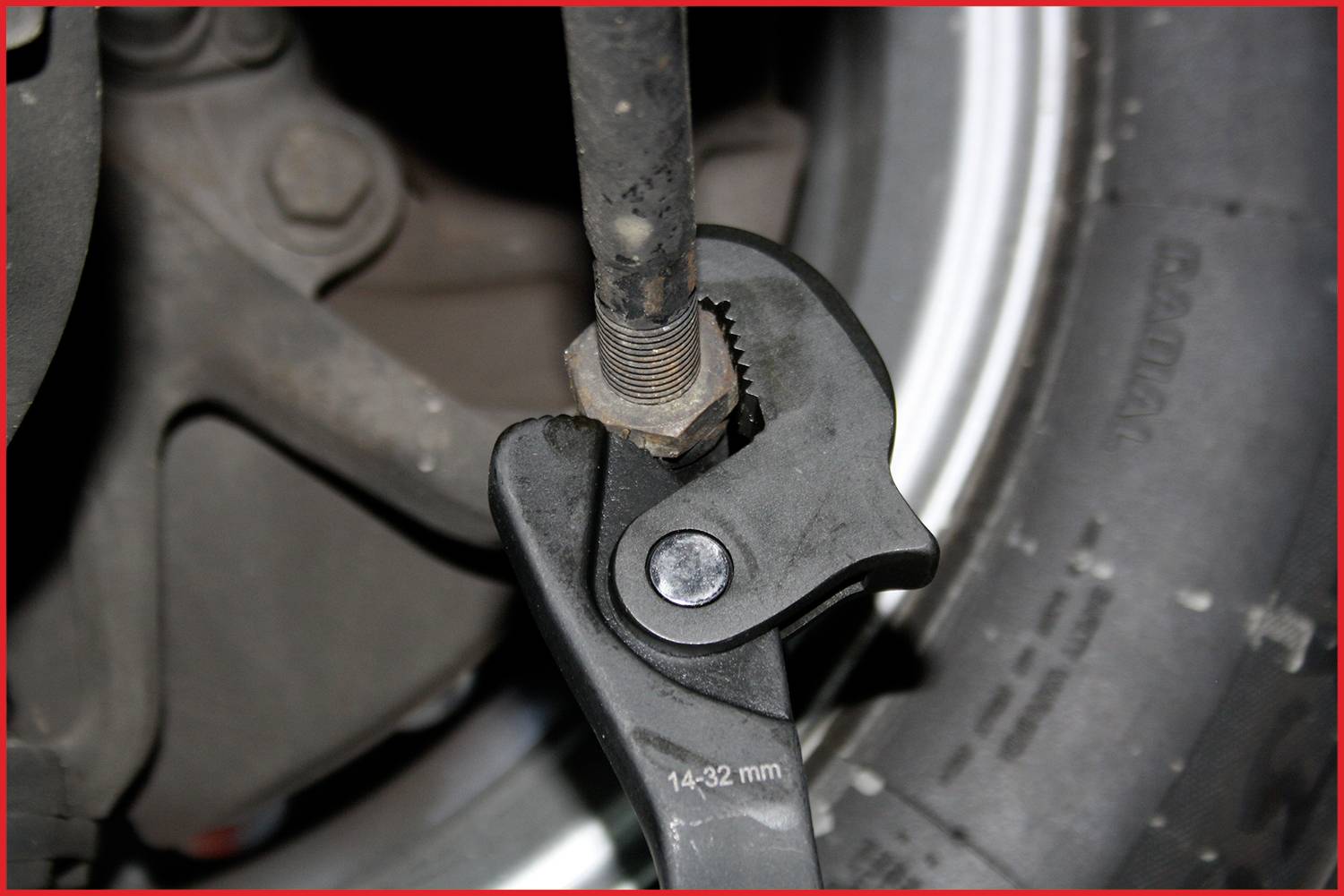 Francúzsky kľúč uťahuje maticu na tyči, ktorá je umiestnená pred pneumatikou a automobilovým dielom.