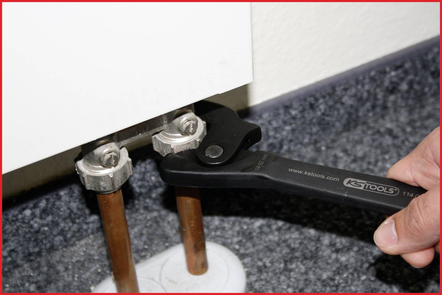 Osoba dotiahuje spoj dvoch vodovodných potrubí čiernym stavebným kľúčom.