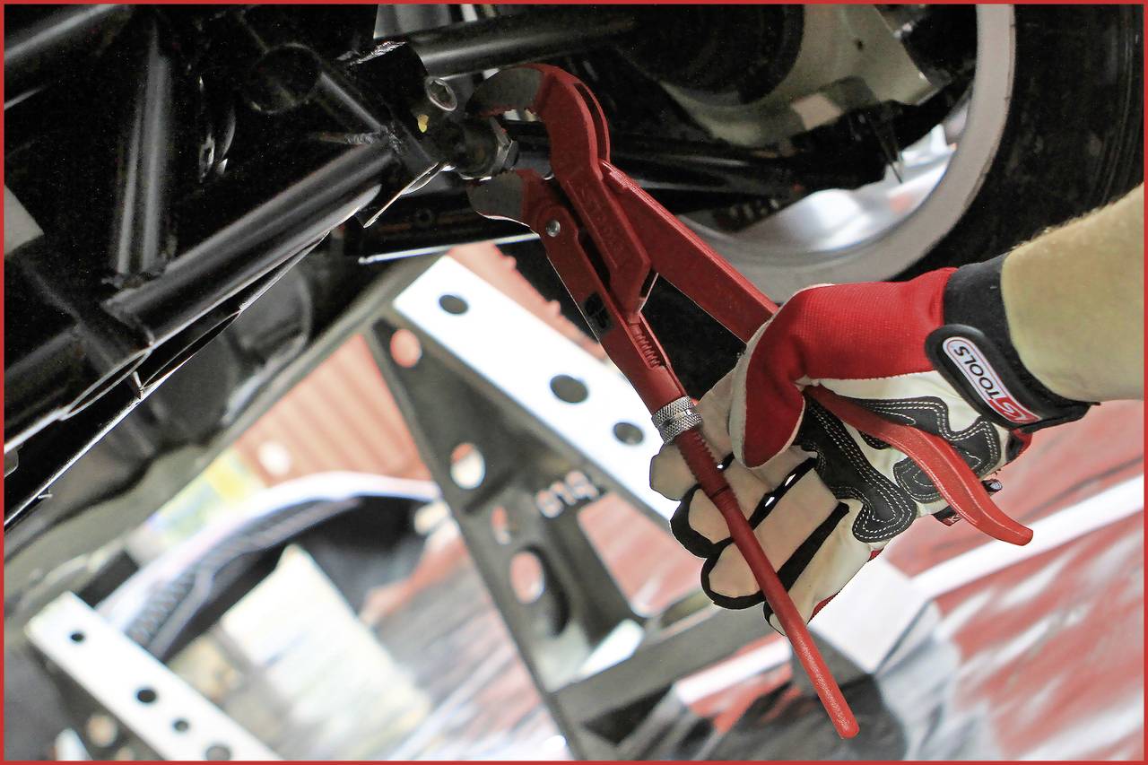 Osoba v pracovných rukaviciach používa červené inštalatérske kliešte na prácu na časti vozidla vo vnútri.