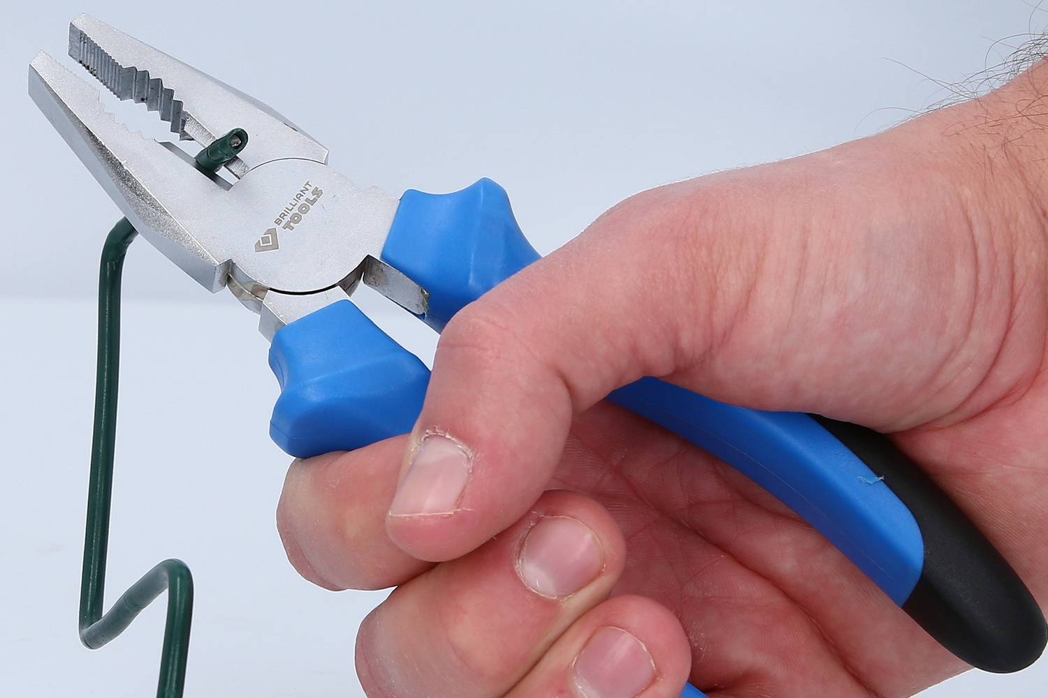 Ruka drží modré kliešte a ohýba zelený drôt.