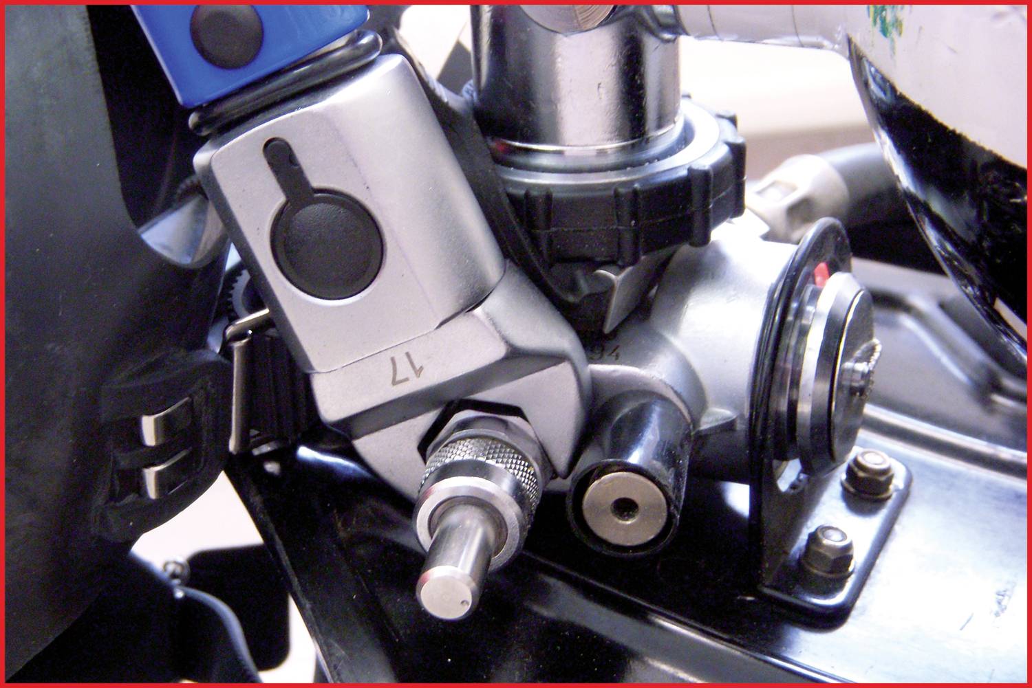 Detailný záber ukazuje časť strojového komponentu s kovovým ramenom a strieborným otočným gombíkom, namontovaným na čiernom kove.