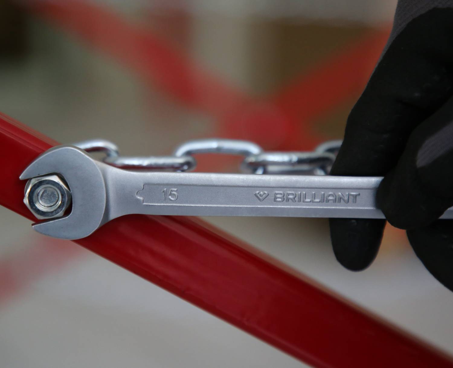 Ruka v rukavici drží kľúč, ktorým uťahuje maticu na červenej kovovej konštrukcii.