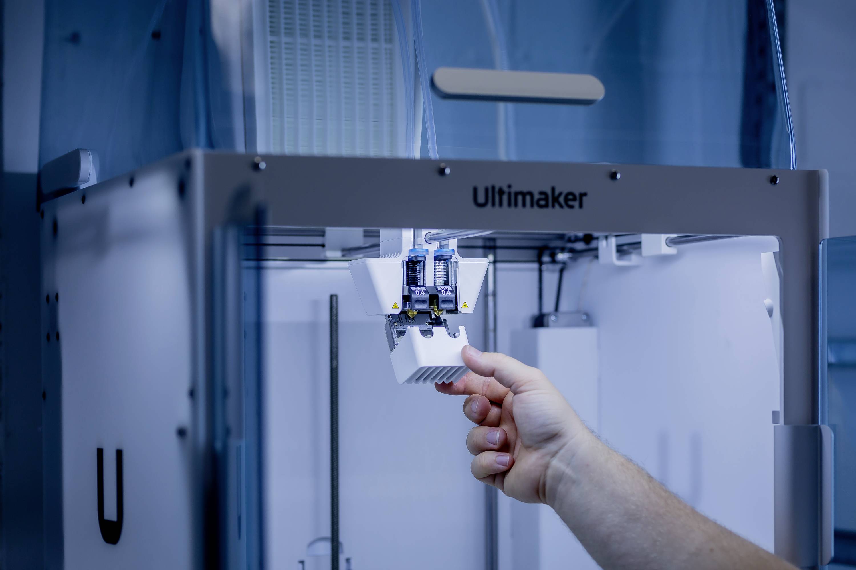 Osoba obsluhuje 3D tlačiareň v laboratóriu. Nastavuje súčiastku vo vnútri tlačiarne.