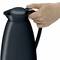 Jedna ruka drží čiernu termosku za jej rukoväť. Veko je pevne uzavreté.