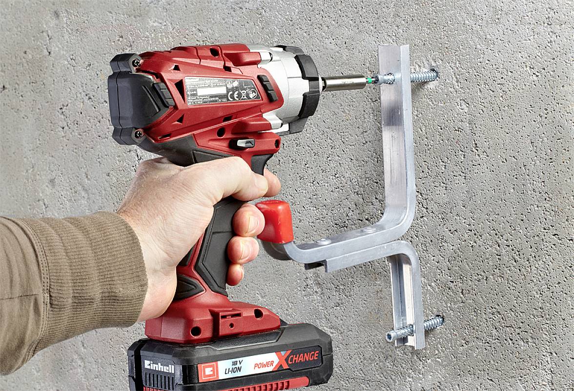 Osoba upevňuje kovovú konzolu na betónovú stenu pomocou červeného akumulátorového skrutkovača.