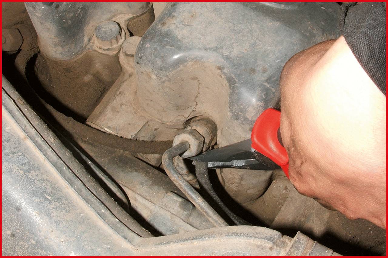 Ruka drží kľúč a uťahuje skrutku na silne znečistenom povrchu pripomínajúcom motor.